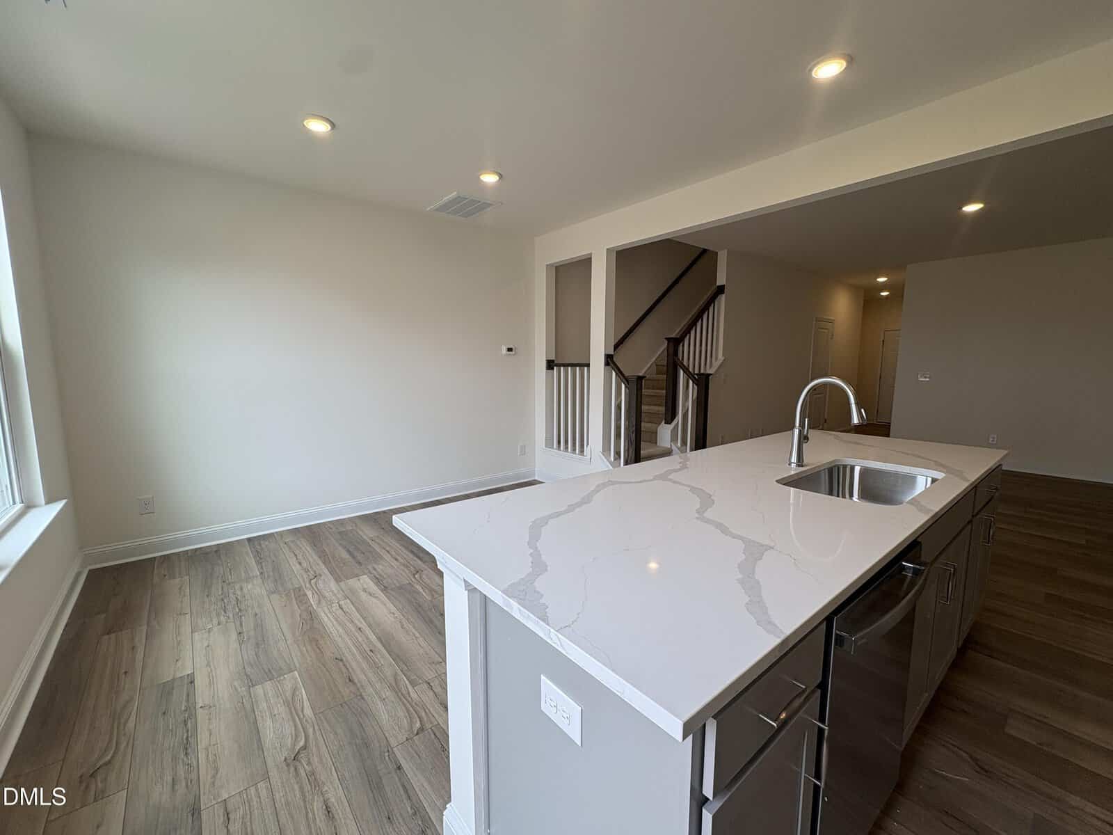 A modern kitchen island with a white quartz countertop and stainless steel sink faces a staircase with dark wood banisters and white spindles.