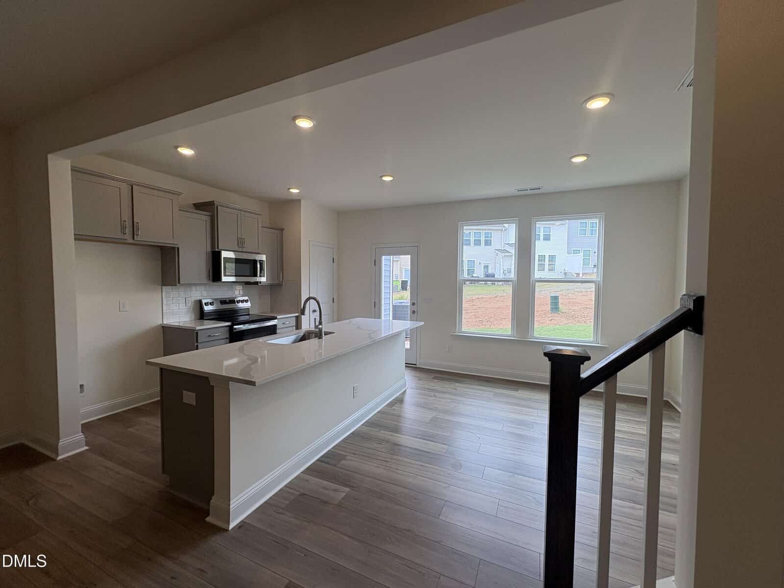 Open-concept kitchen and living area with gray cabinets, quartz island, stainless steel appliances, subway tile backsplash, hardwood floors, recessed lighting, and windows overlooking a neighborhood.