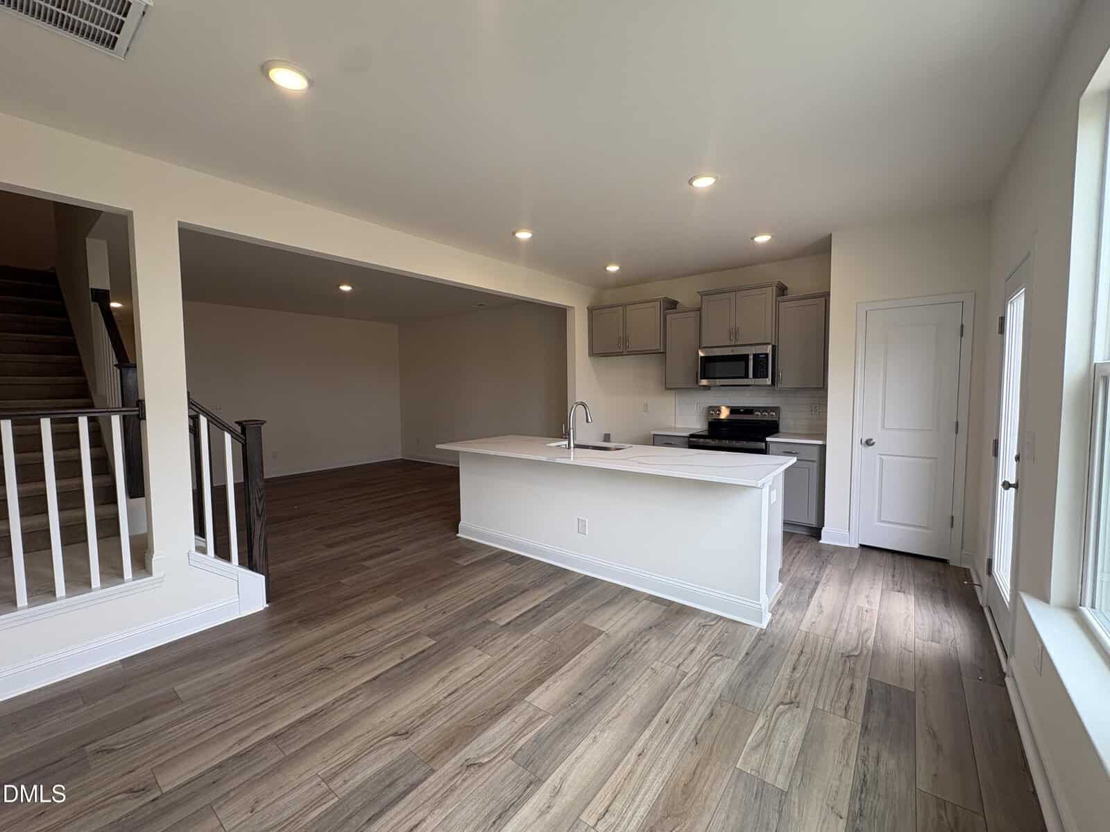 A spacious open-concept living area with a modern kitchen, white island, and adjacent living room. The kitchen features gray cabinets and stainless steel appliances.