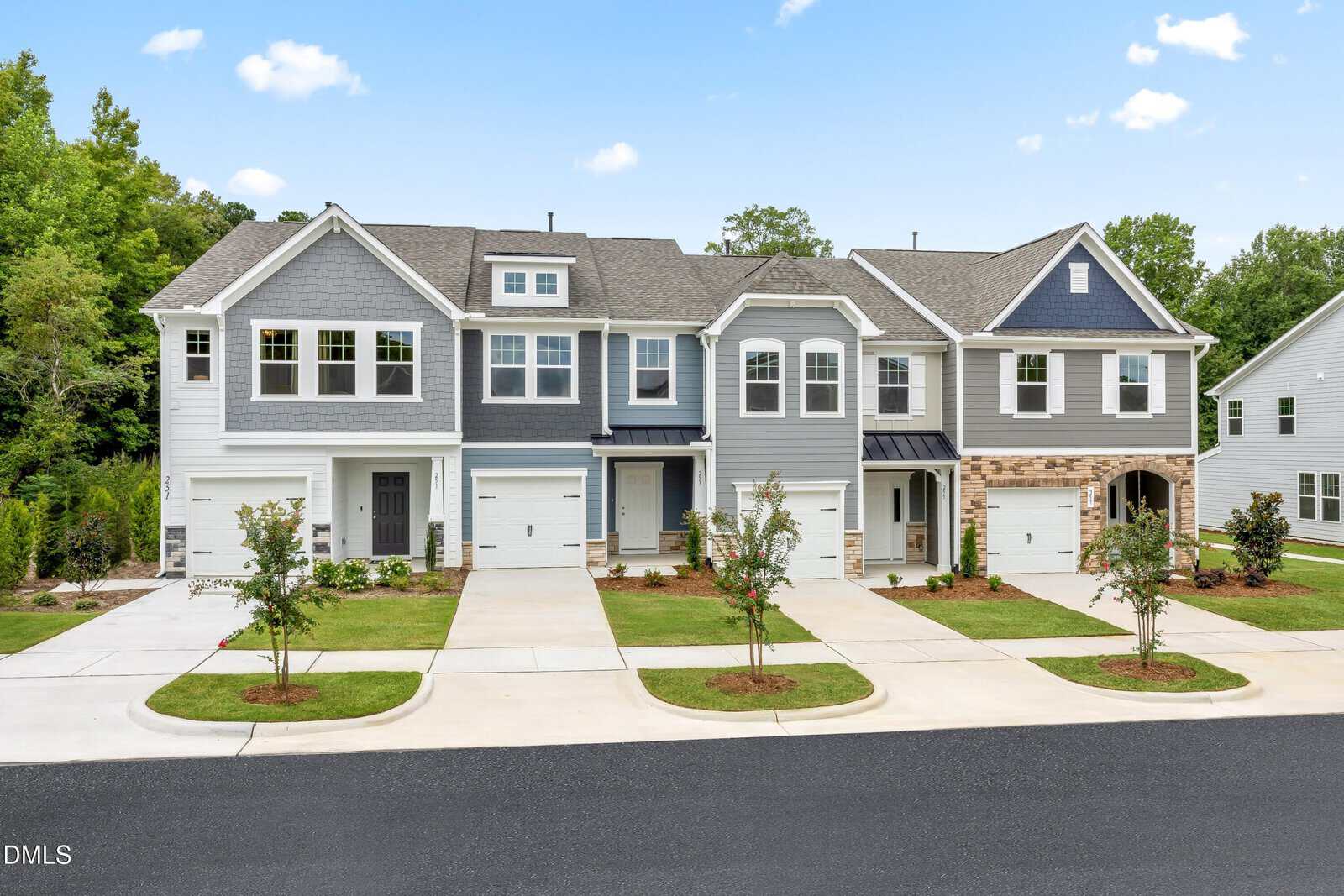 A row of new, modern two-story townhouses with garages and small front lawns sits under a blue sky with scattered clouds on 221 Alberta Drive in Franklinton. Trees and other houses are visible in the background.
