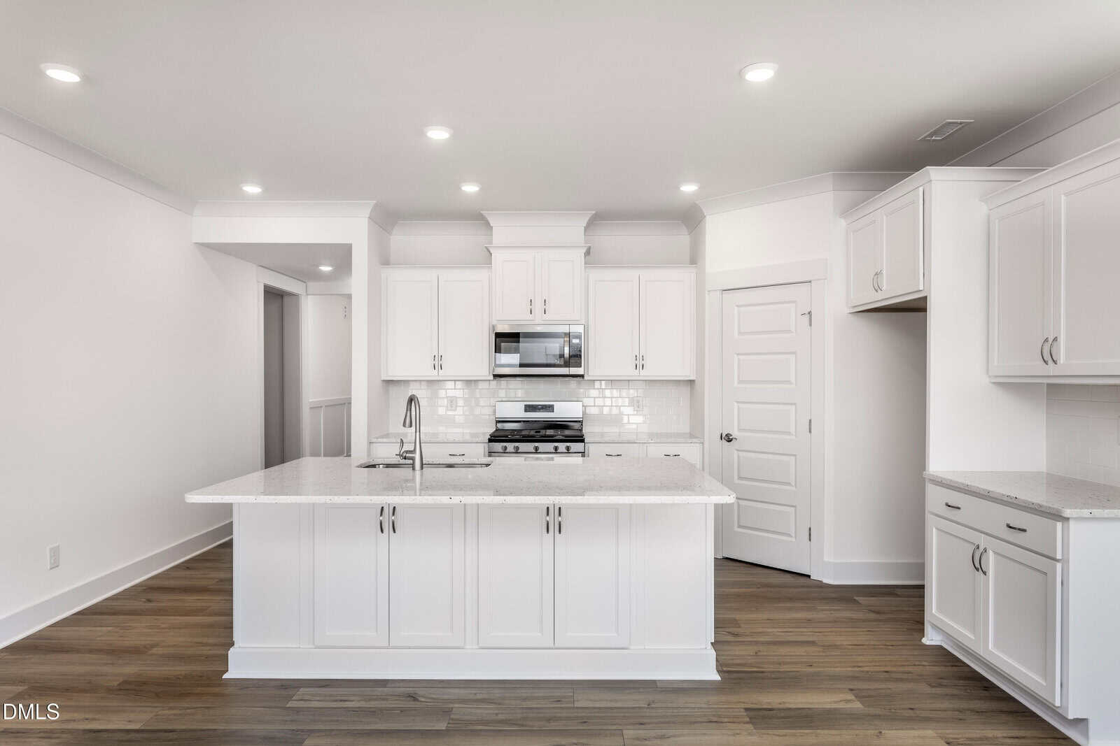 Modern kitchen with white cabinets, stainless steel appliances, a central island with a sink, subway tile backsplash, and light wood flooring. The space is bright with recessed ceiling lights.