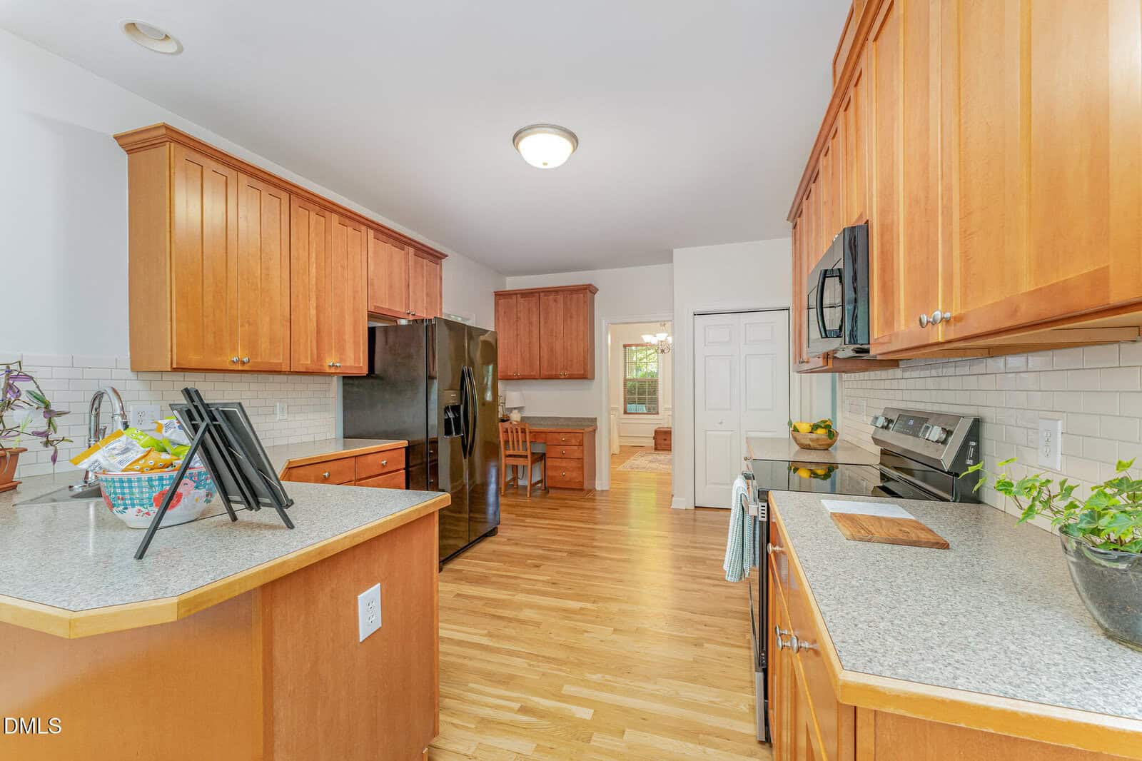A spacious kitchen with light wood floors, wooden cabinets, stainless steel appliances, white subway tile backsplash, and a center island. A small dining area is visible in the background.