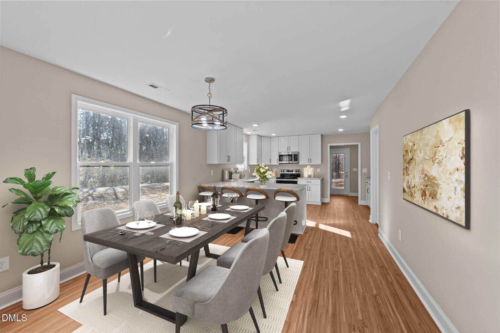 Bright dining area with a dark wooden table, six gray chairs, and a modern chandelier. Open kitchen in the background with white cabinets, barstools, and stainless steel appliances. Large windows and a potted plant add light.