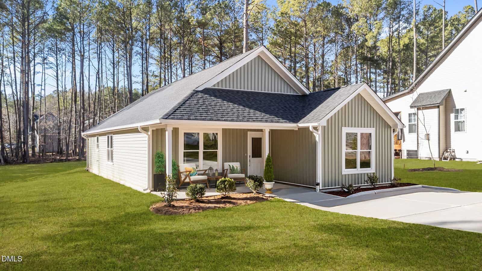 Charming single-story house at 108 Wichita Way, Louisburg, with gray siding, white trim, and a dark roof. Enjoy the covered front porch, landscaped yard, concrete driveway, and pine trees set under a clear blue sky.