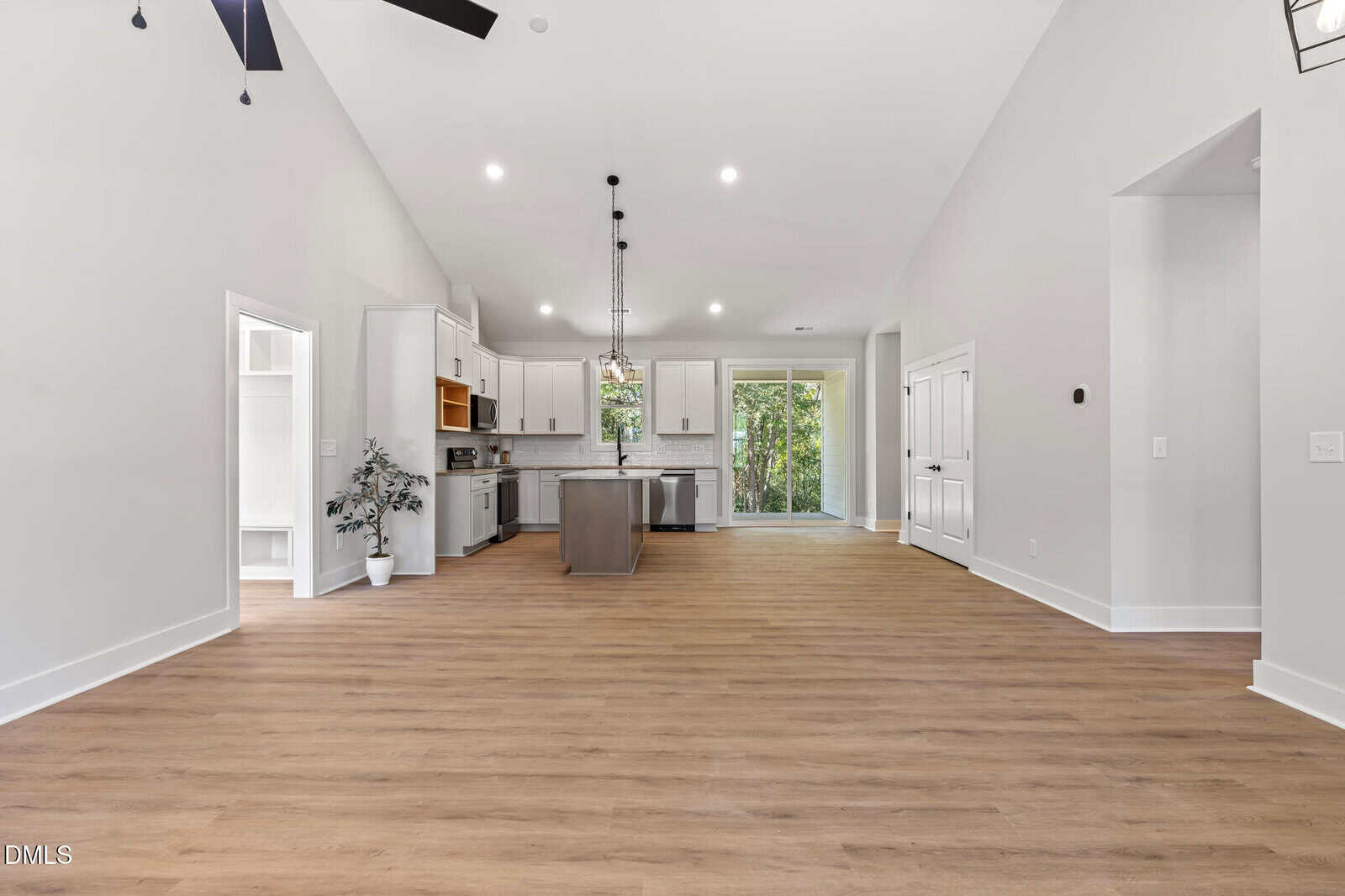 Open concept kitchen and living area with wood floors, white cabinets, center island, pendant lights, sliding glass doors, and adjacent rooms visible.