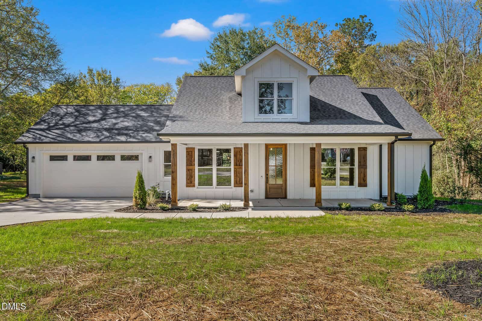 A modern white house with black roof on 321 W Noble Street in Louisburg features a covered front porch, wood columns, large windows, and attached two-car garage, surrounded by grass and trees under a blue sky.
