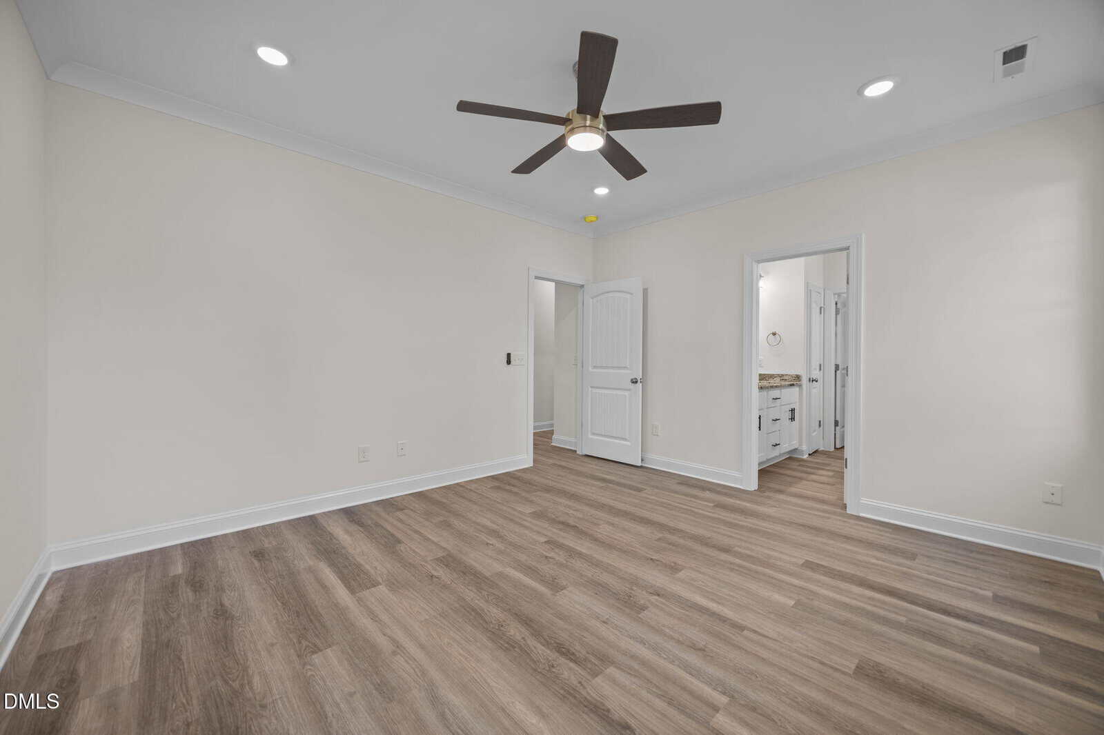 A spacious, empty room with light-colored walls, wood-look flooring, a ceiling fan, and two open doorways leading to a bathroom and closet. Recessed lighting is installed in the ceiling.