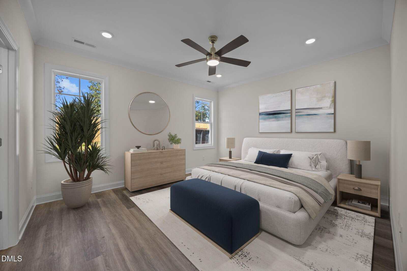 Modern bedroom with light walls, wood flooring, and a large bed with neutral bedding and a blue bench. Room features two windows, a dresser with a round mirror, potted plant, and two abstract paintings above the bed.
