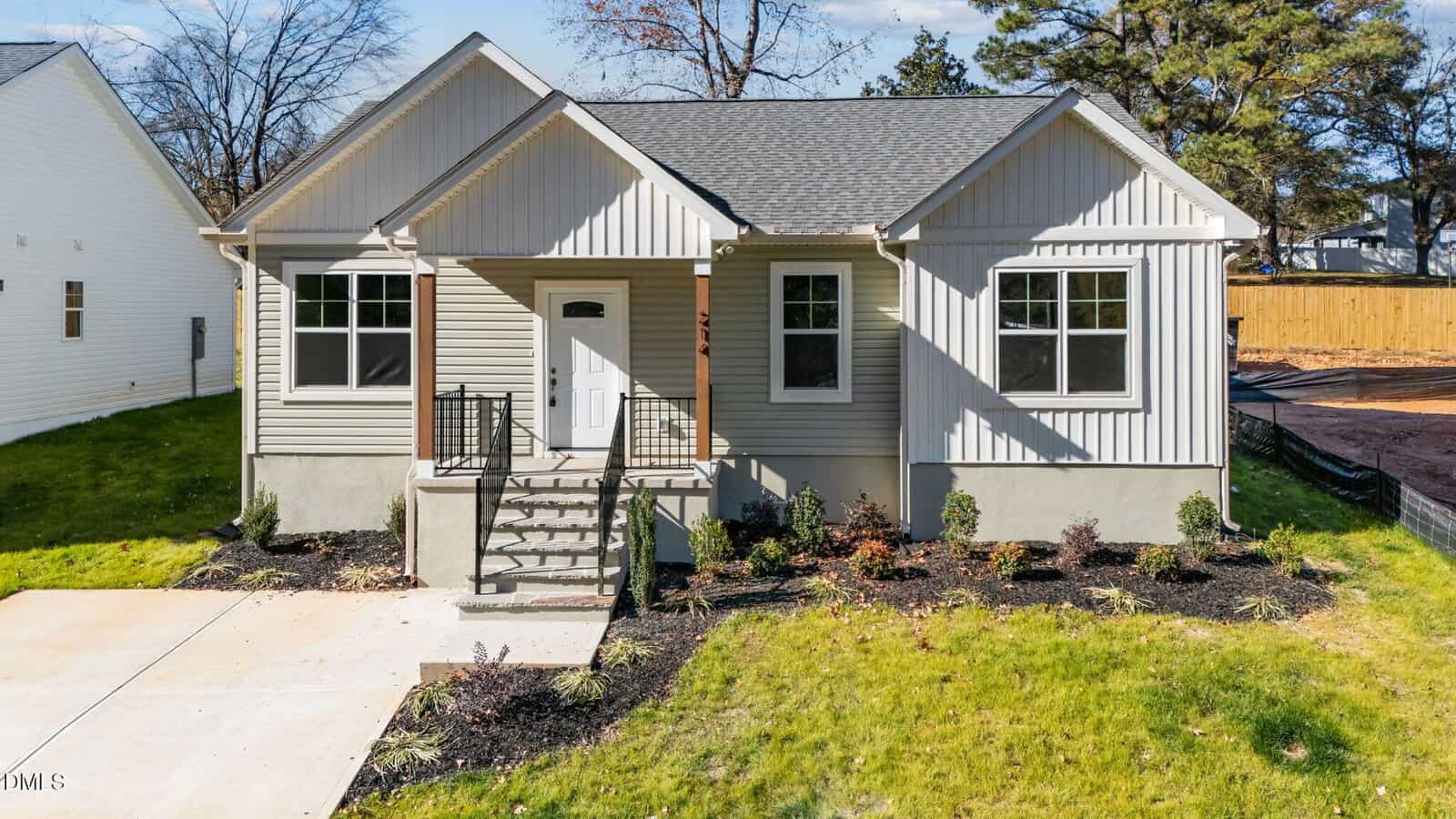 A small, modern, single-story house with light gray siding and a gabled roof sits at 214 E College Street in Franklinton. Enjoy a front porch with steps, neatly landscaped yard, green grass, shrubs, and a concrete driveway.