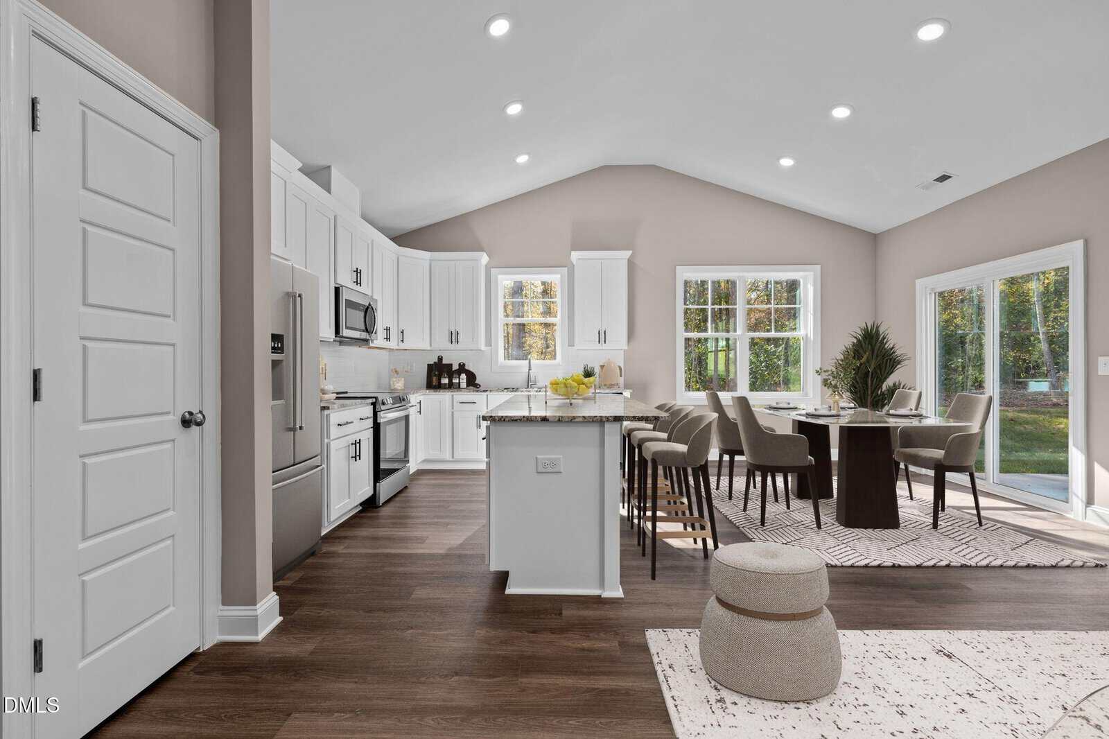 Modern open-concept kitchen and dining area with white cabinets, stainless steel appliances, large island with stools, dining table with chairs, and large windows letting in natural light. Light walls and dark wood flooring.