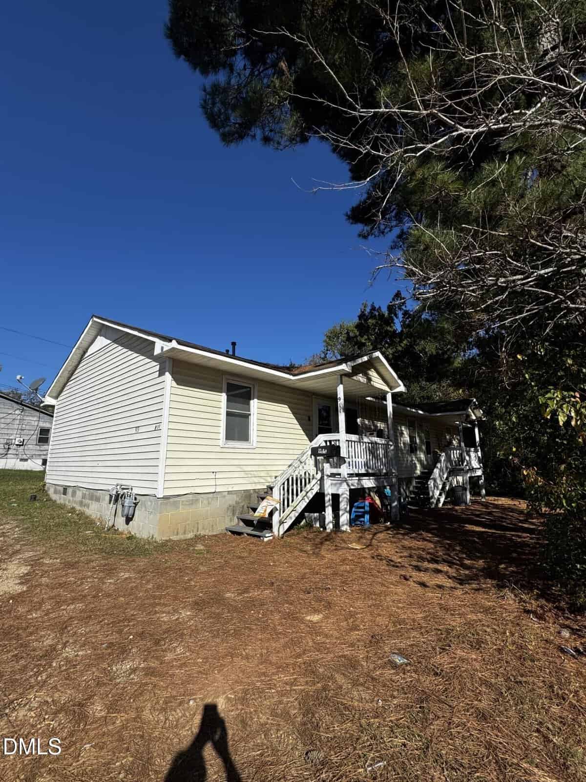 A small, single-story beige house with white trim and a covered front porch sits on a raised foundation at 911/913 Water in Henderson. Steps lead up to the porch, while a pine tree and dry ground are visible in the foreground.