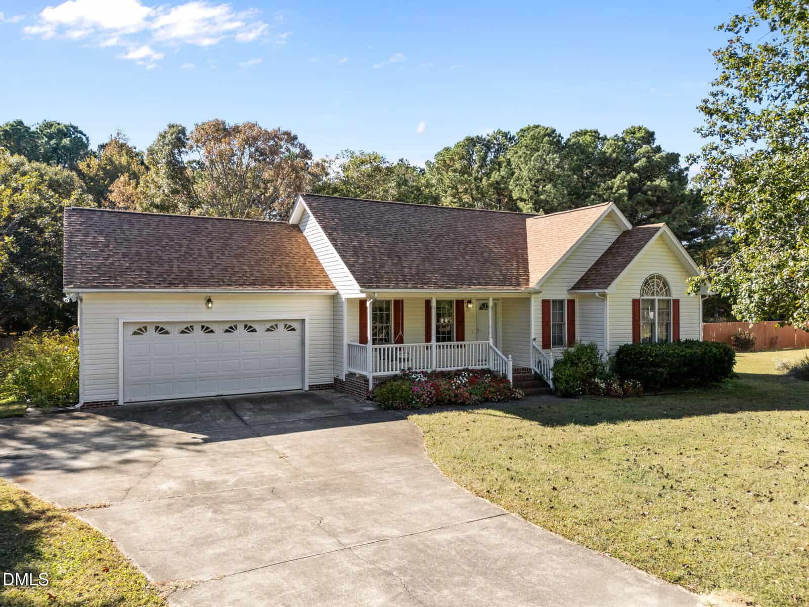 Charming single-story house at 45 Prestwould Drive in Youngsville, featuring a covered front porch, attached two-car garage, classic gable roof, and crisp white siding. A curved concrete driveway leads to the home, which is surrounded by a well-maintained lawn with shrubs and trees in the background.