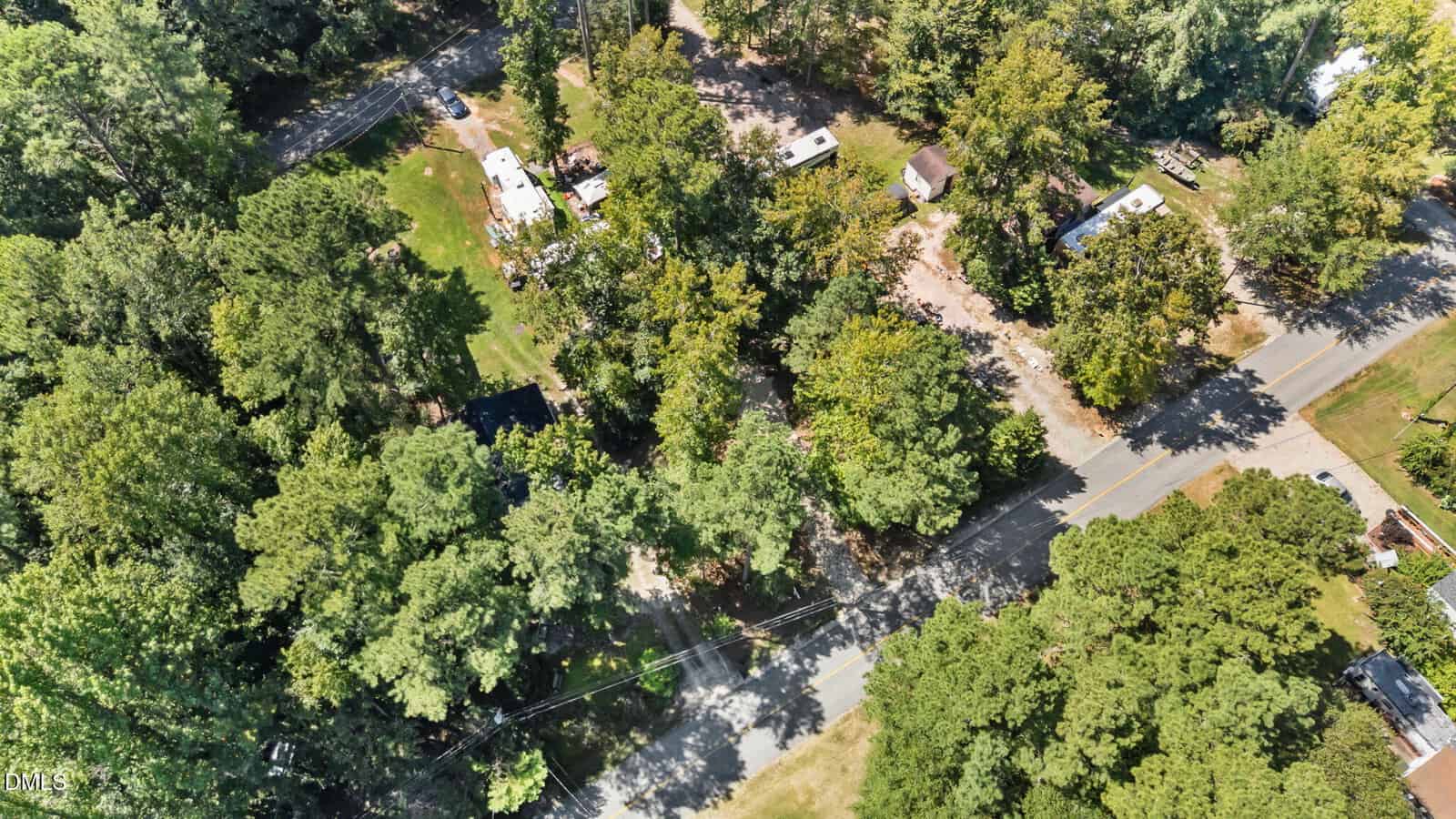 Aerial view of a wooded area with several RVs and small buildings among trees, next to intersecting roads. The scene includes dense greenery and some clearings.