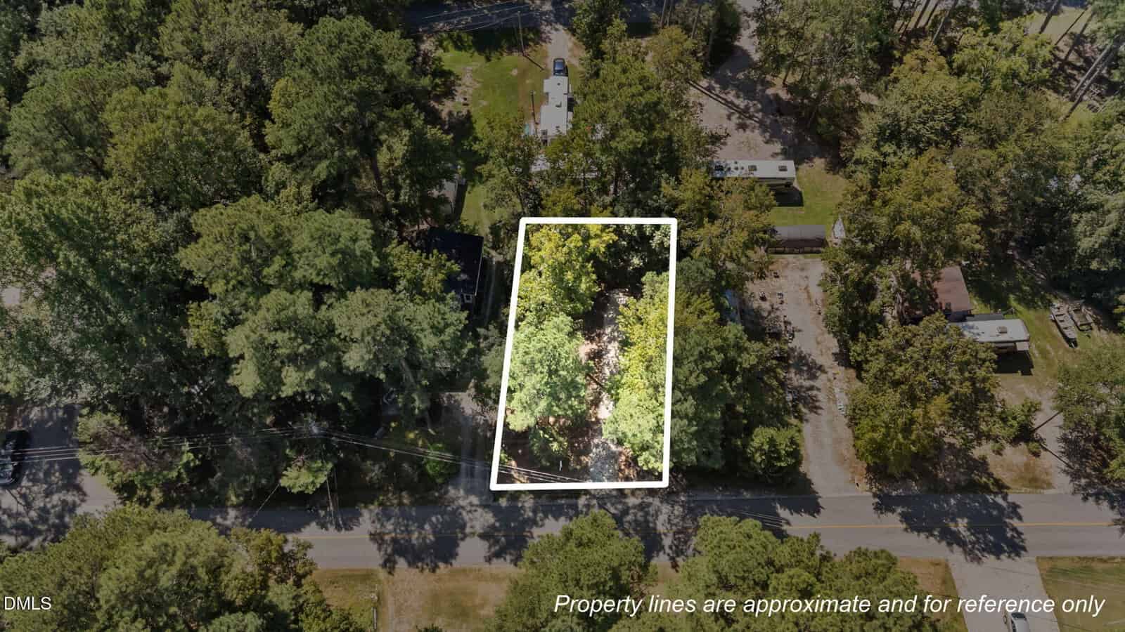 Aerial view of a tree-filled lot bordered by white lines, indicating approximate property boundaries. The lot sits along a paved road, surrounded by more trees and nearby homes. Text states boundaries are for reference only.