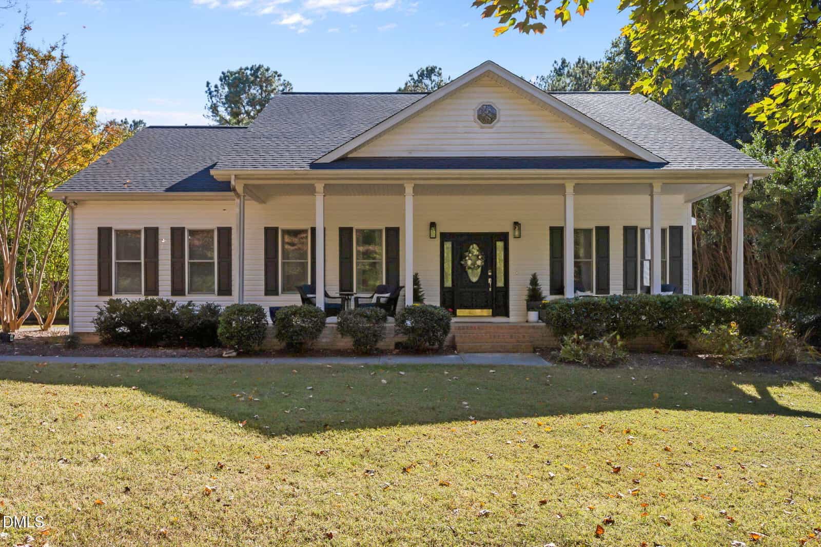 Charming single-story house at 15 Marlowe Drive in Youngsville featuring a covered front porch, white siding, black shutters, four columns, and a glass front door. The yard is grassy with shrubs along the porch and trees in the background.