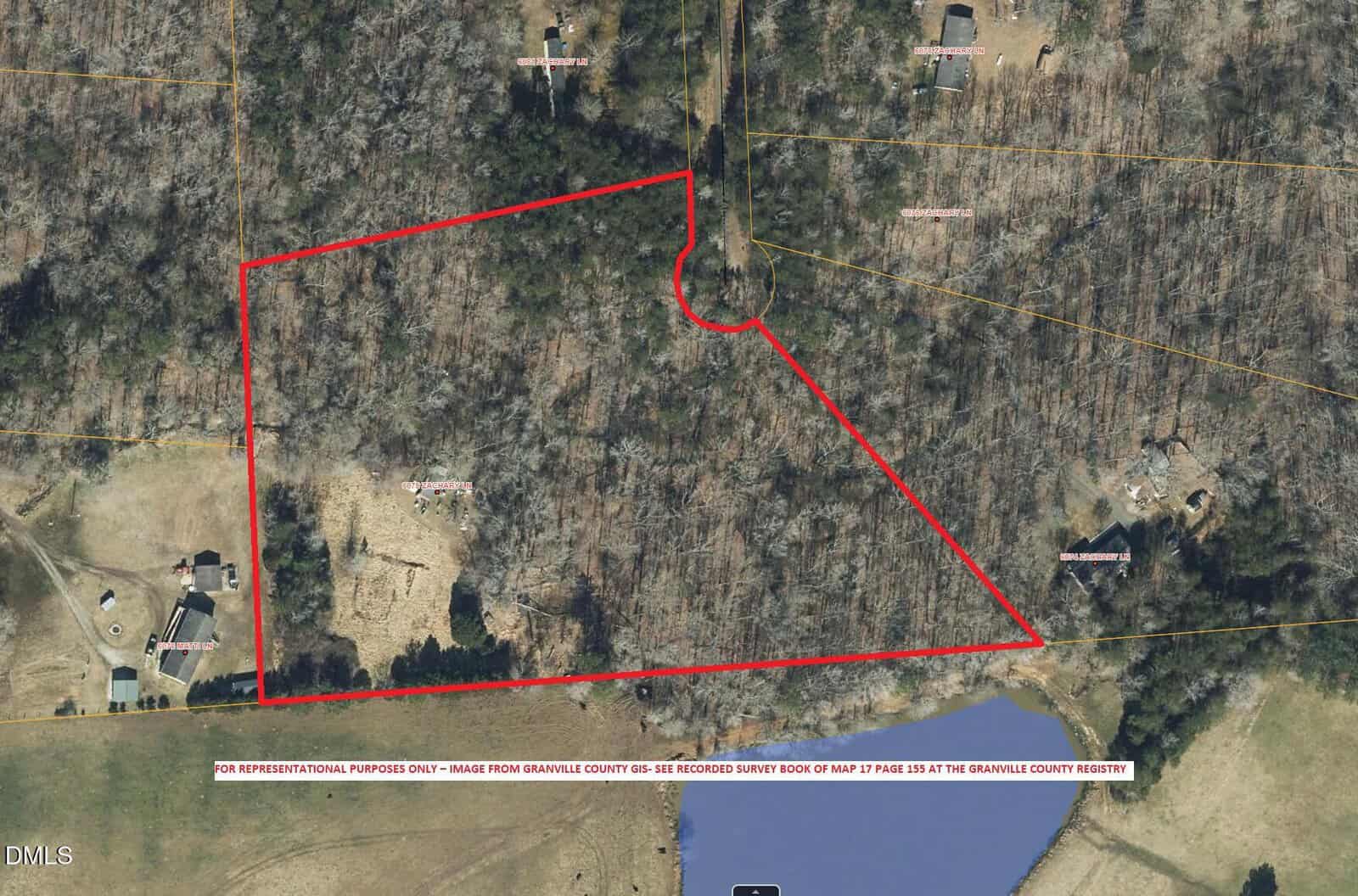 Aerial view of a wooded area outlined in red near Oxford, with a cul-de-sac and several houses on 6079 Zachary Lane. Roads, property lines, and a pond at the bottom edge are visible. The landscape is mostly rural.