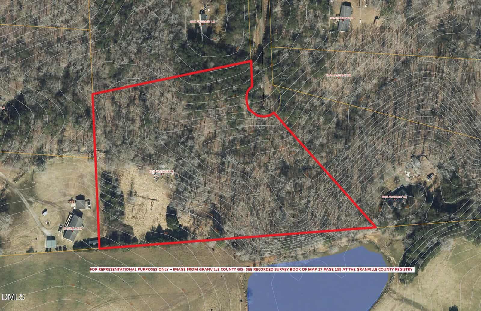 Aerial view of a property outlined in red, showing wooded and cleared areas, nearby structures, a pond at the bottom right, and contour lines indicating elevation changes across the landscape.
