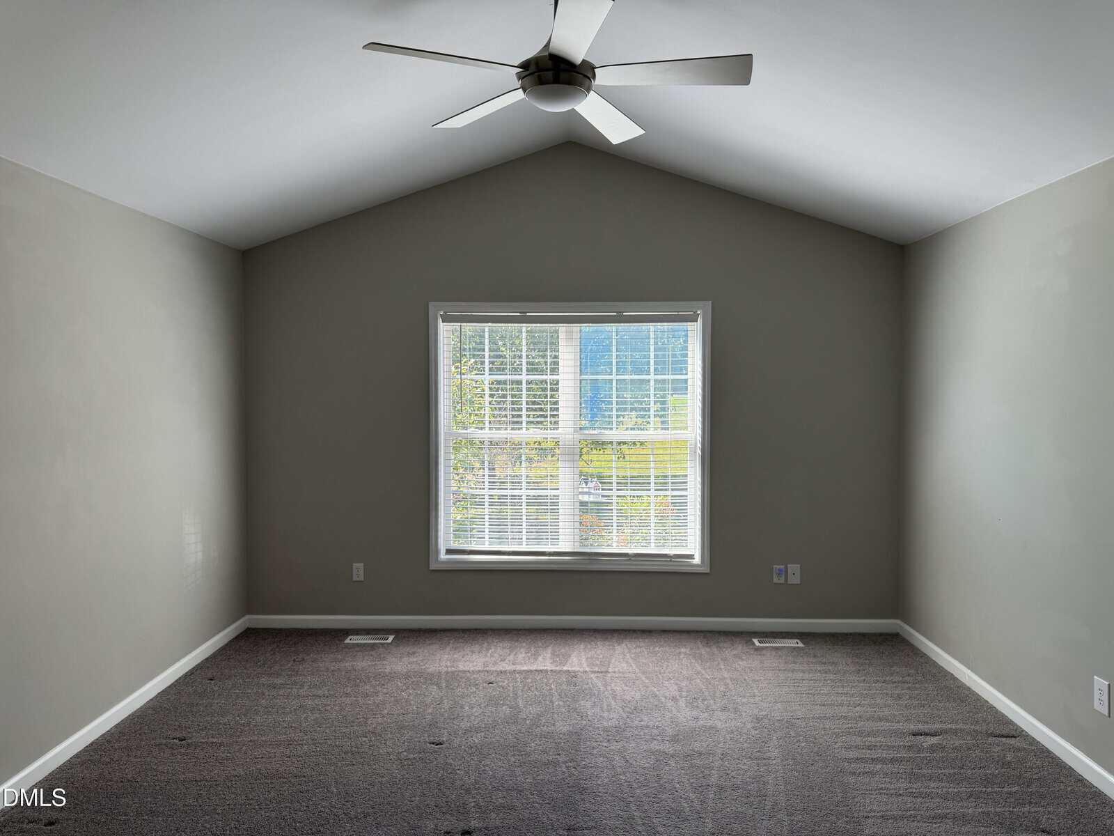Empty room with gray walls, dark carpet, a ceiling fan, and a large window with white blinds letting in natural light.