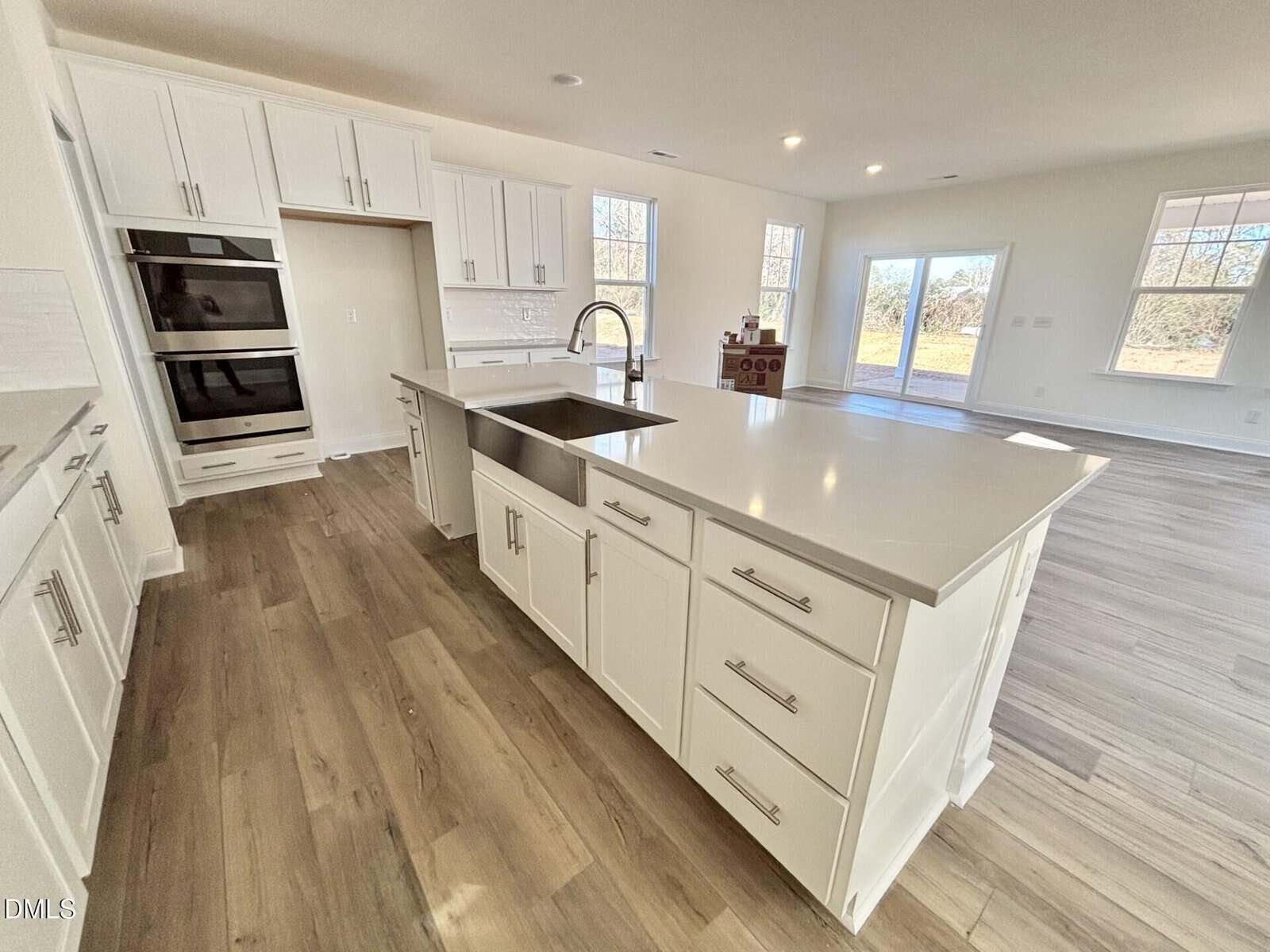 Modern kitchen with white cabinets, stainless steel appliances, a large island with a sink and faucet, light wood flooring, and large windows letting in ample natural light.