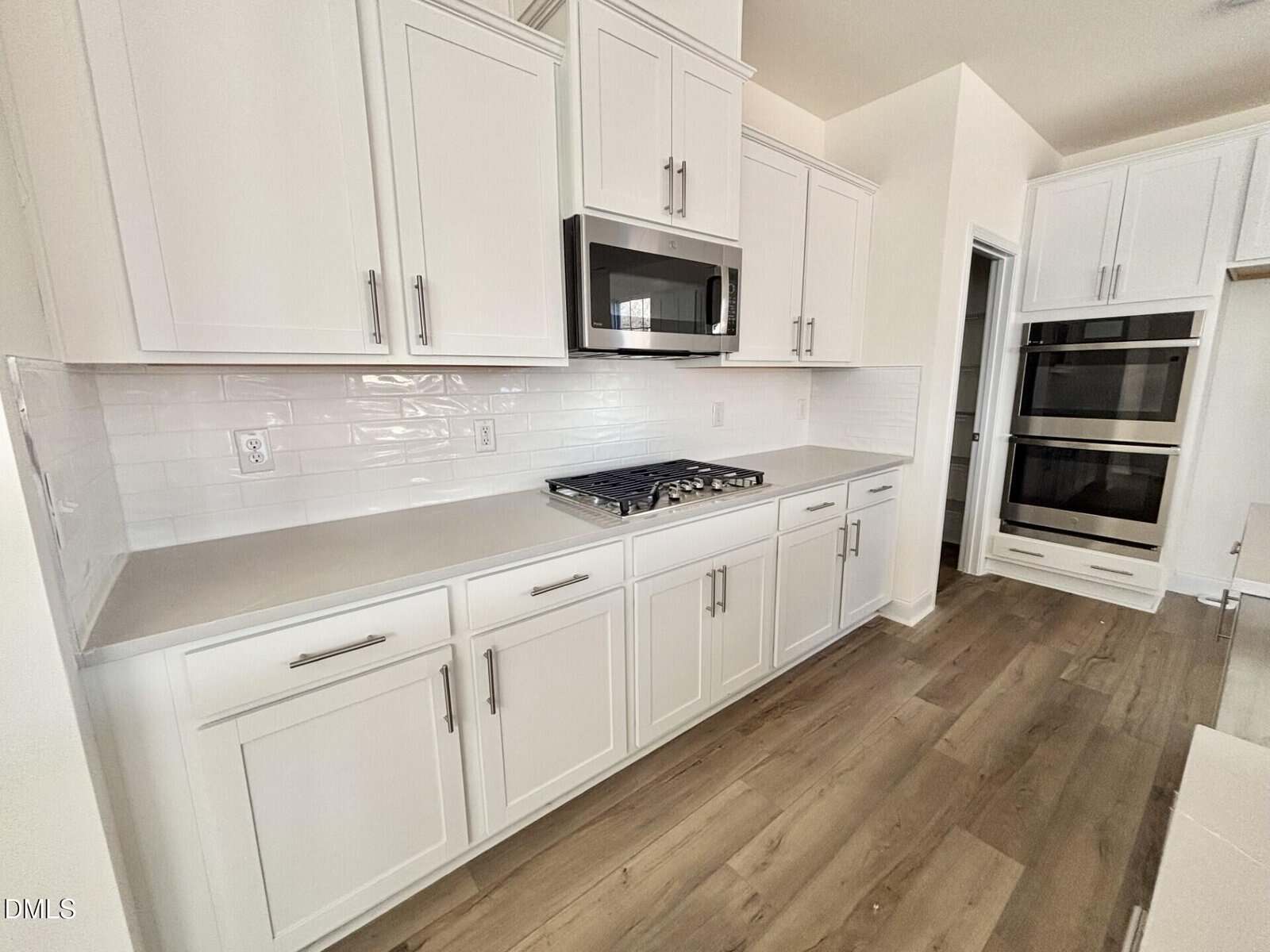Modern white kitchen with shaker cabinets, stainless steel appliances including a built-in microwave, oven, and gas cooktop, white subway tile backsplash, and light wood flooring.