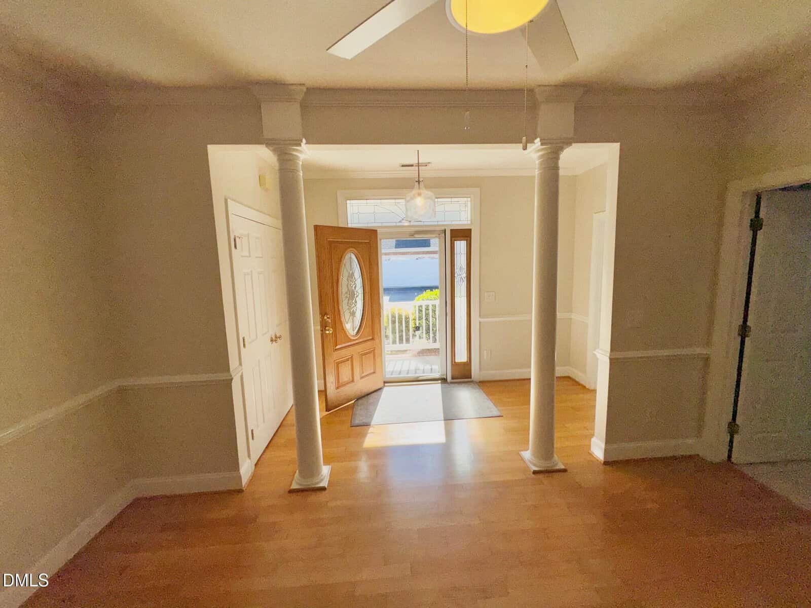 A bright entryway at 105 Fernwood Creek Court features light wood floors, white walls, two white columns, an open wooden door with glass panel, and natural light streaming in from a window above the door in Henderson. A ceiling fan is partially visible.