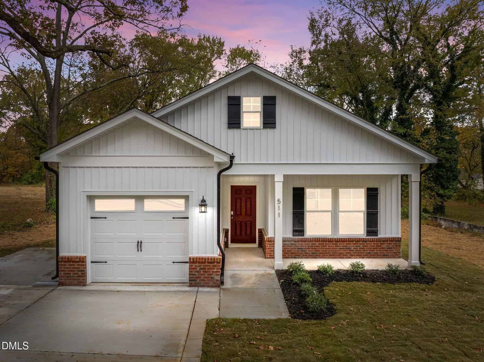 A single-story house on 511 Broad Street in Oxford features white siding, brick accents, a front porch with columns, a dark red front door, and an attached garage, set against trees and a pink and purple sunset sky.