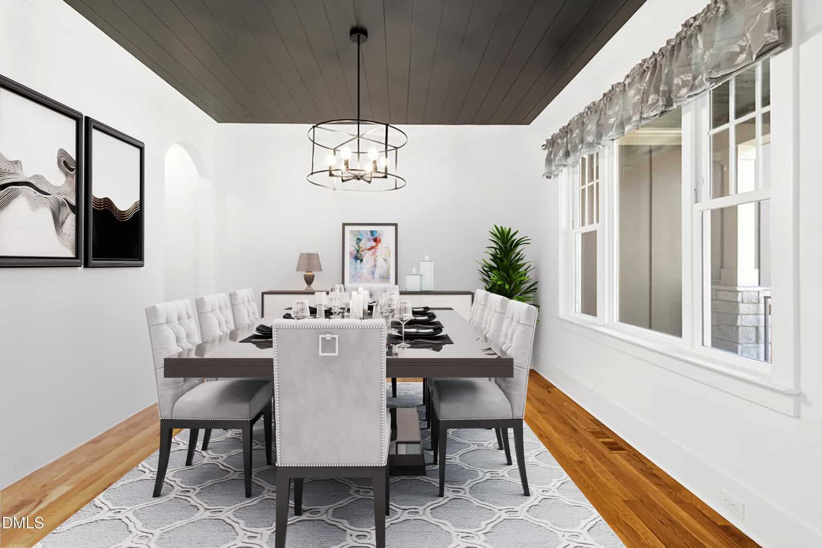 A modern dining room with a dark ceiling, rectangular table set for eight, gray upholstered chairs, light patterned rug, artwork on white walls, hardwood floors, and a large window with sheer curtains.