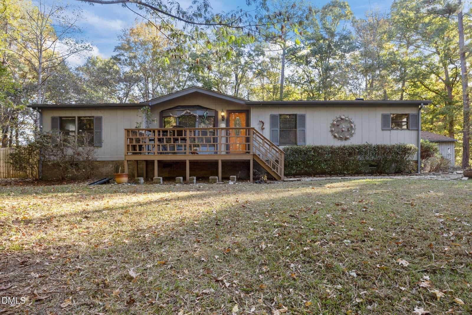 A single-story house on 1644 Fawn Lane in Creedmoor features light gray siding, a wooden front porch and steps, and a large decorative wreath. Surrounded by trees, grass, and fallen leaves, it offers cozy charm in every season.