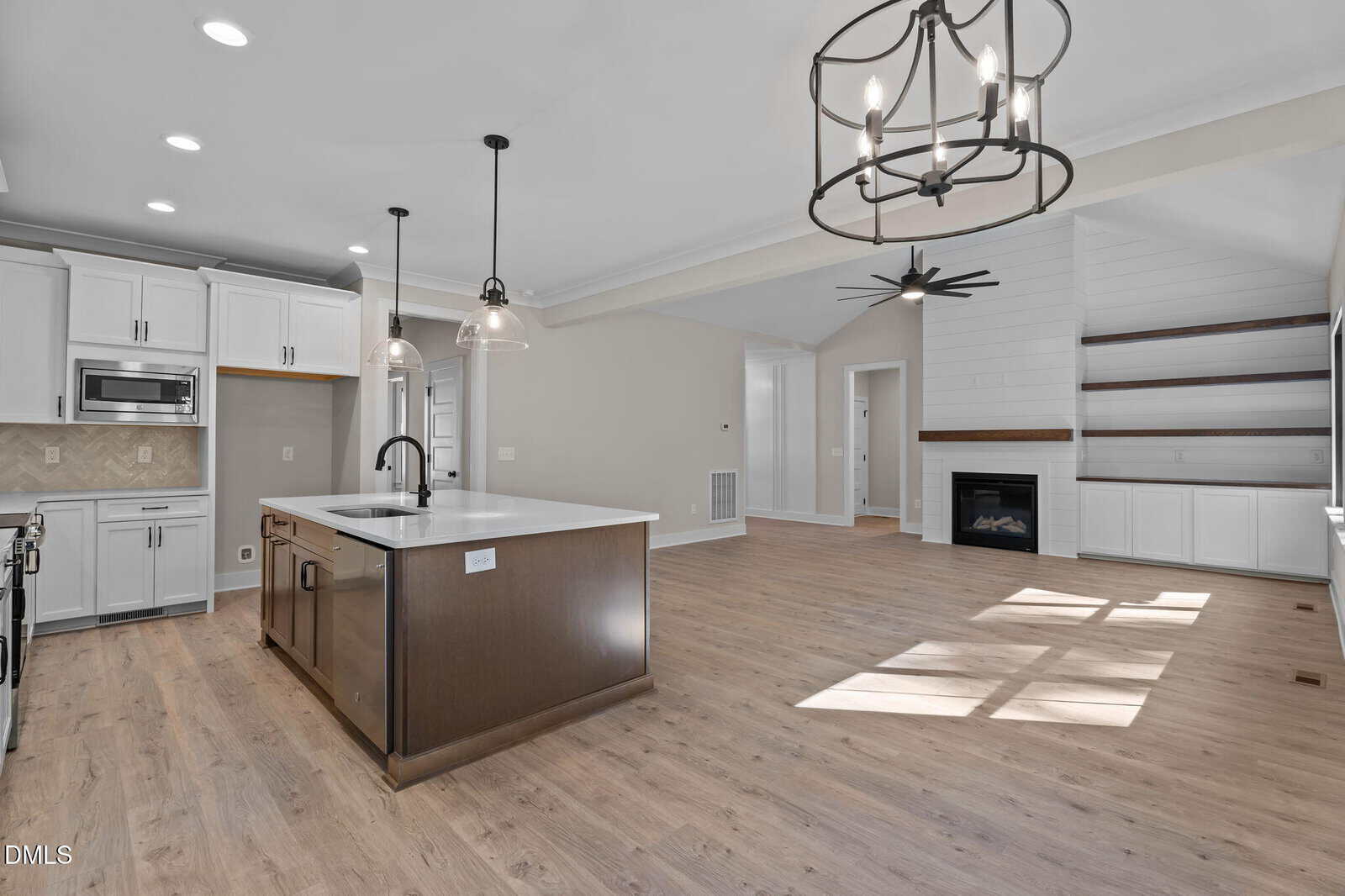 Open-concept kitchen and living room with white cabinets, a center island, pendant lights, wood floors, built-in shelves, a fireplace, and large windows letting in natural light.