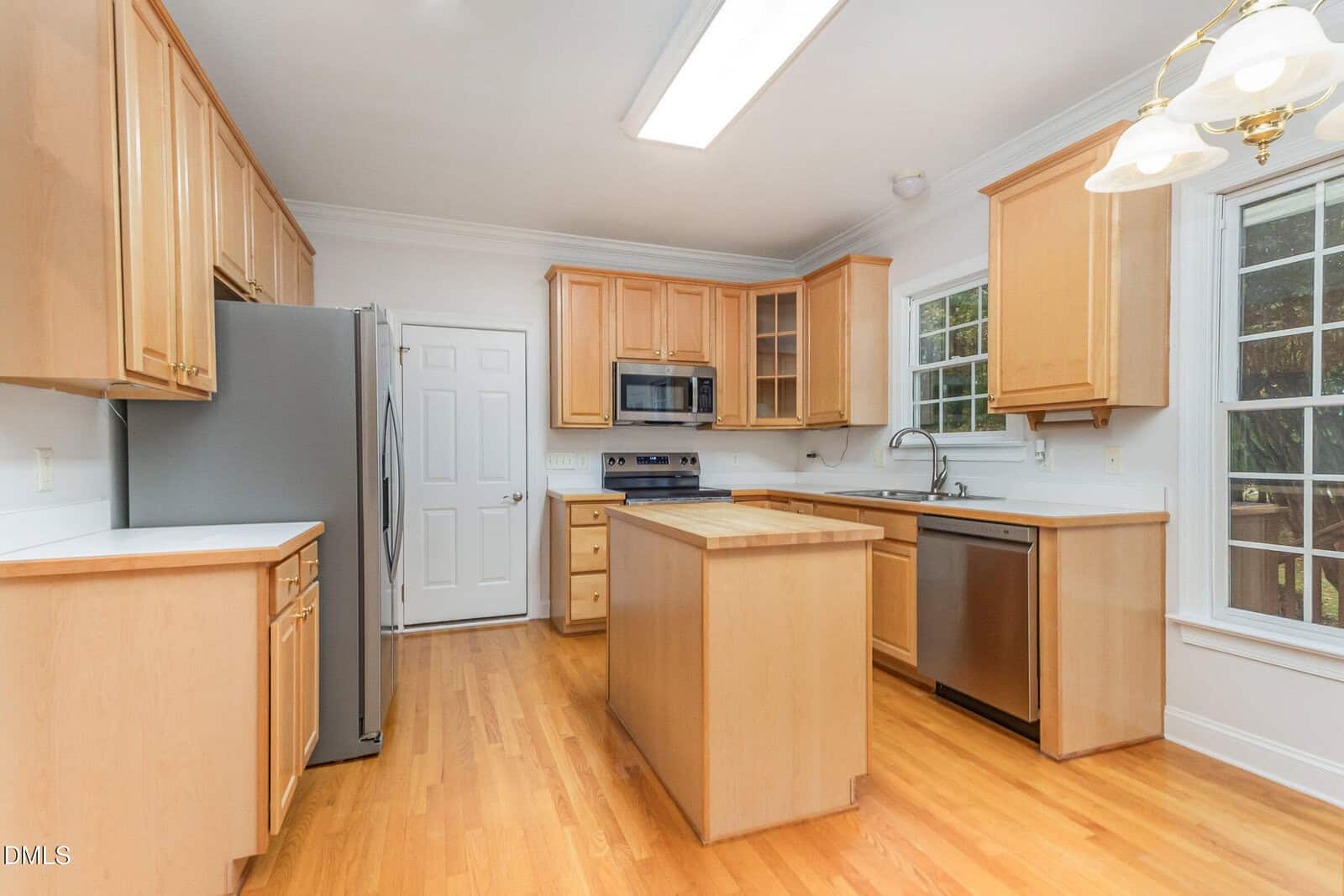 Bright kitchen with light wood cabinets, stainless steel appliances, center island, white countertops, large window for natural light, and hardwood floors.