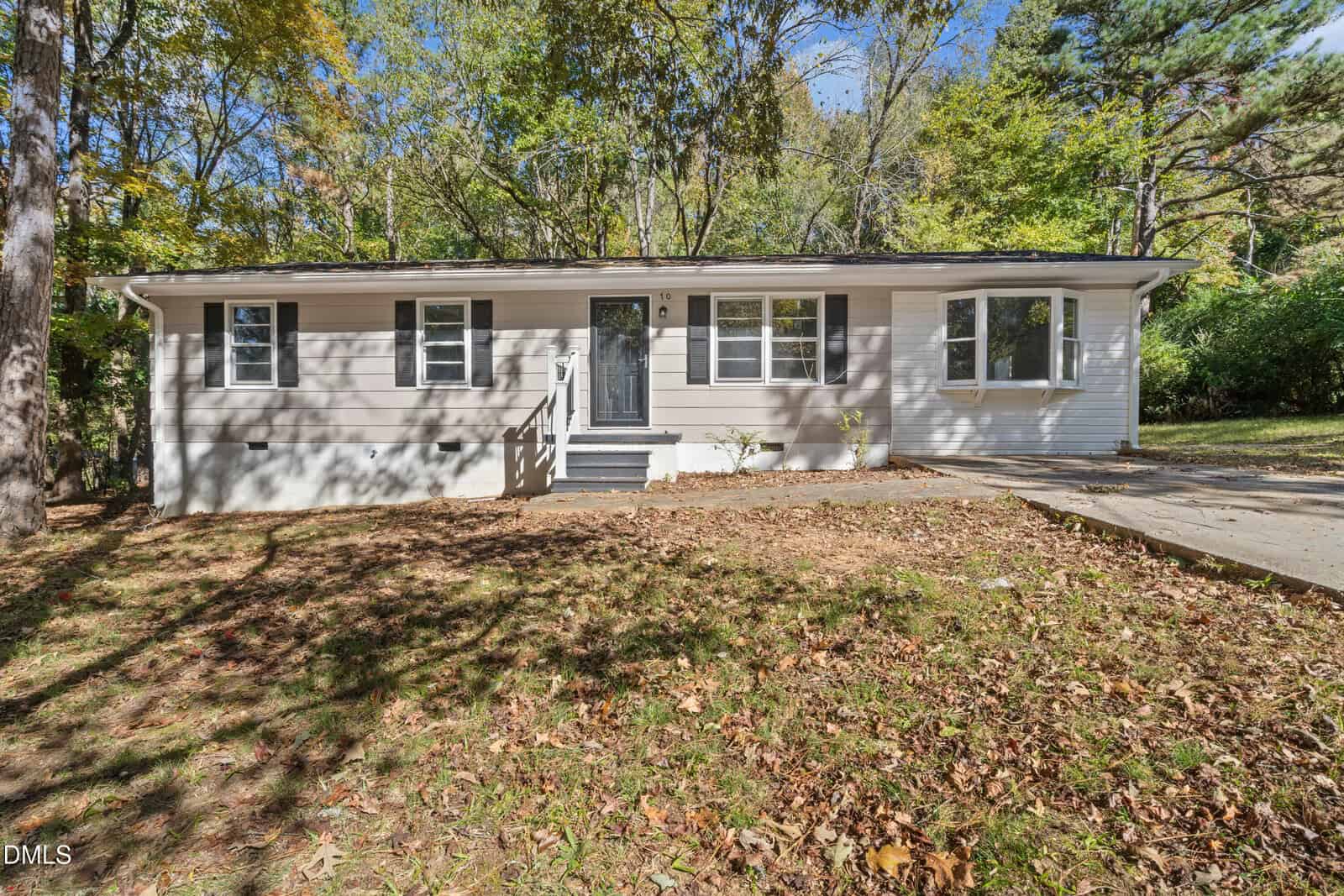 Charming single-story house at 70 Lynnbank Estates Road in Kittrell features light gray siding, white trim, a dark front door, and multiple windows. Nestled among trees, the yard is blanketed with fallen leaves and a driveway sits to the right.