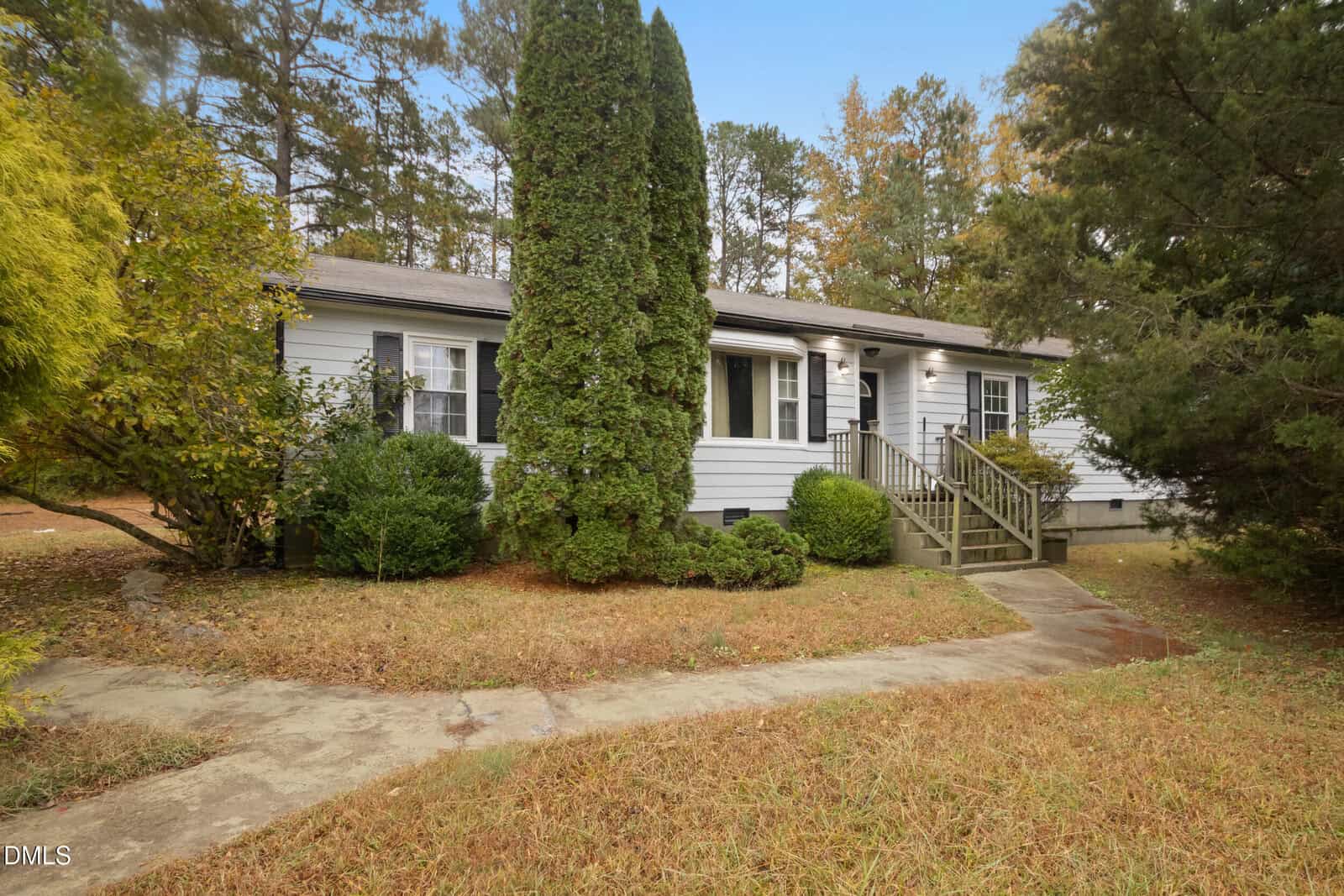 Charming single-story white house at 2930 Thomas Road, Henderson, with black shutters, a front porch with steps, and trees and shrubs surrounding the yard. Dry grass covers the lawn, and a curved concrete walkway leads to the entrance.
