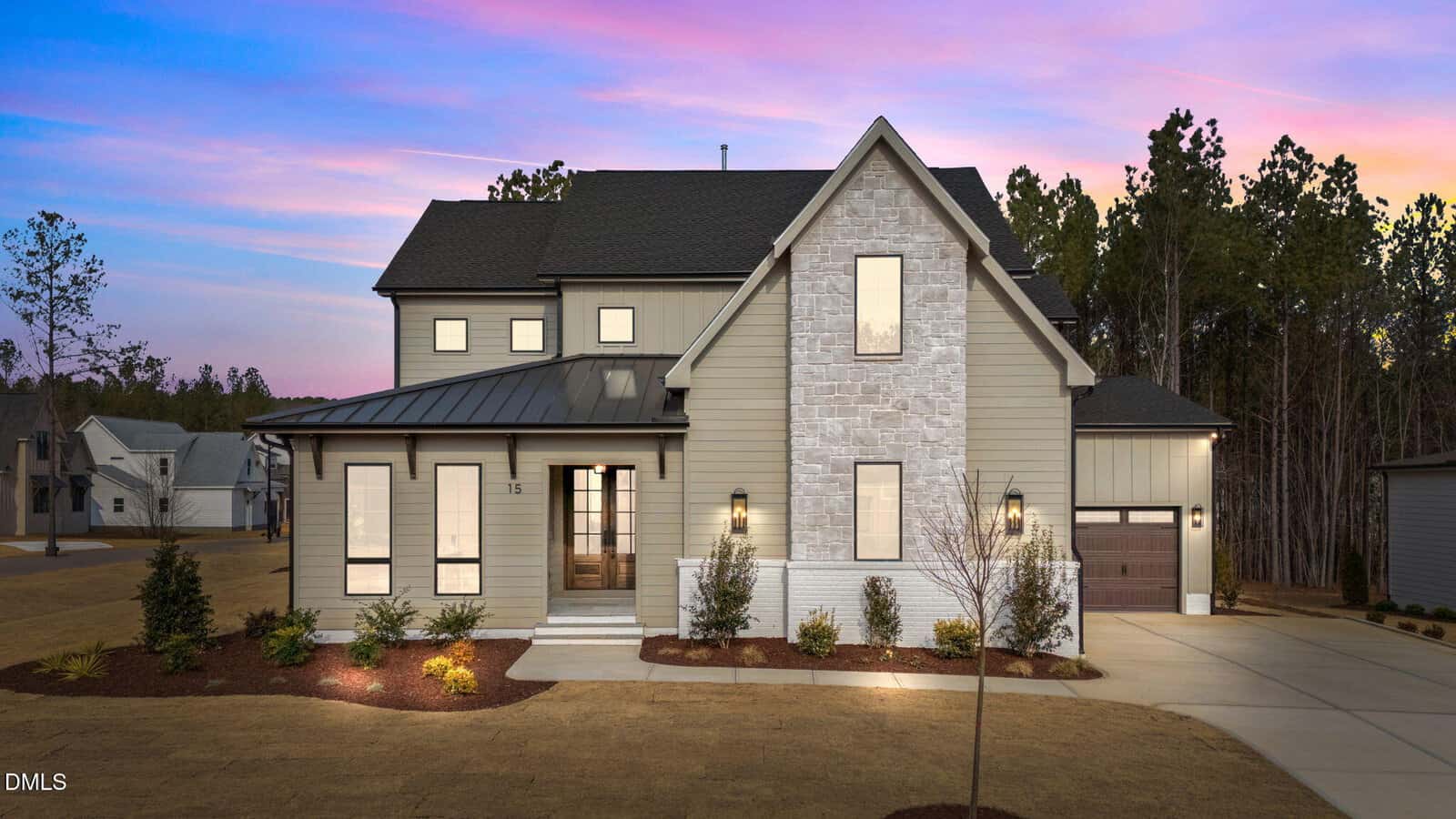 A two-story modern suburban house at 15 Chestnut Oak Drive, Youngsville, features beige siding, large windows, a stone accent wall, and a black roof. The home glows at dusk with a driveway, garage, and minimal landscaping in the front yard.