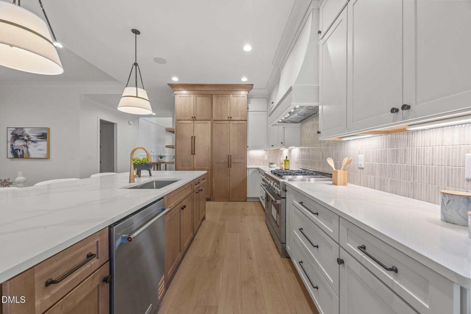 Modern kitchen with white and wood cabinets, stainless steel appliances, marble countertops, a farmhouse sink, pendant lights, and light wood flooring. The kitchen looks spacious and bright with a clean, minimalist design.