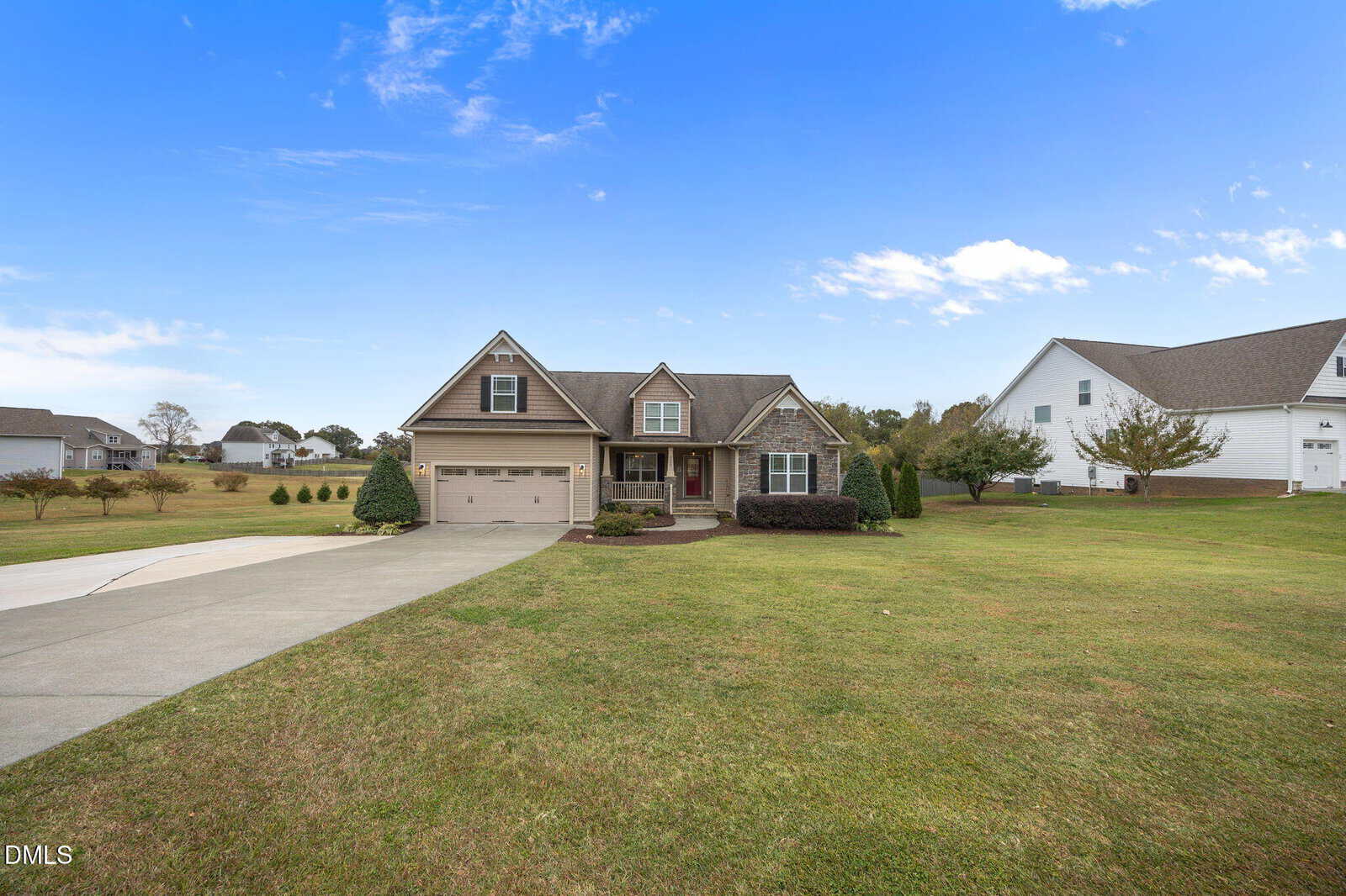 A two-story suburban house with a covered front porch, attached garage, and well-maintained front lawn sits under a partly cloudy blue sky. The driveway and sidewalk lead to the front entrance.