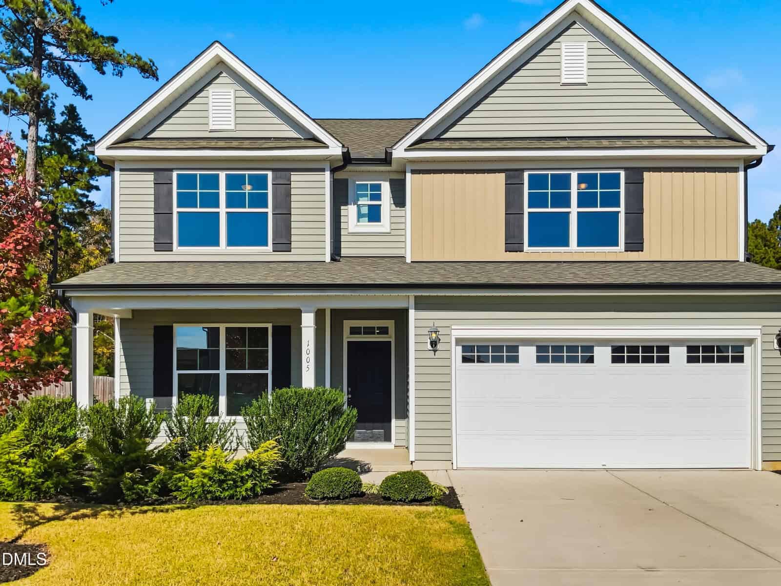 Two-story suburban house with beige siding, black shutters, and a covered front porch located at 1005 Harmony Ranch Lane in Franklinton. There are trimmed bushes near the entrance and a double garage door. The driveway and lawn are visible in the foreground.