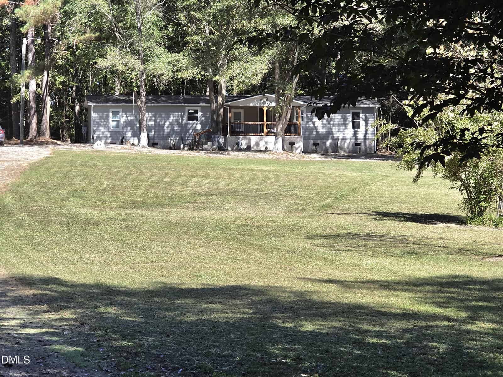 A single-story gray house at 129 Dump Horton Road, Bunn, features a covered front porch and sits at the edge of a large, neatly mowed lawn, surrounded by tall trees and partially shaded by overhanging branches.