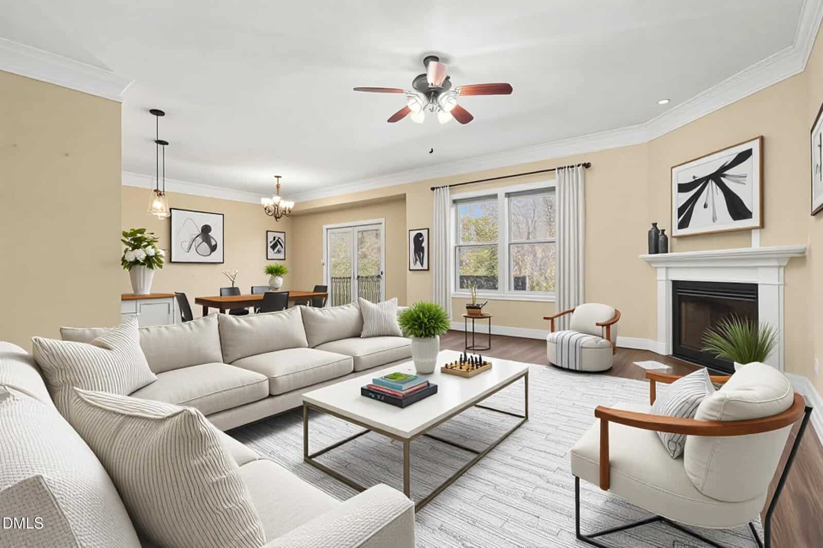 A spacious living room with beige walls, white trim, a white sectional sofa, two accent chairs, a rectangular coffee table, wall art, a fireplace, a ceiling fan, large windows, and a dining area in the background.