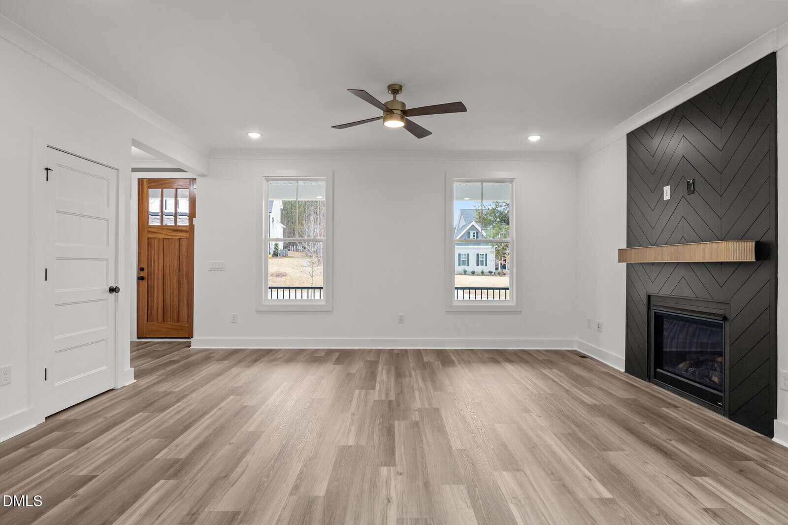 Modern living room with light wood floors, white walls, two windows, a wooden front door, a black accent wall with herringbone pattern, built-in fireplace, and ceiling fan.