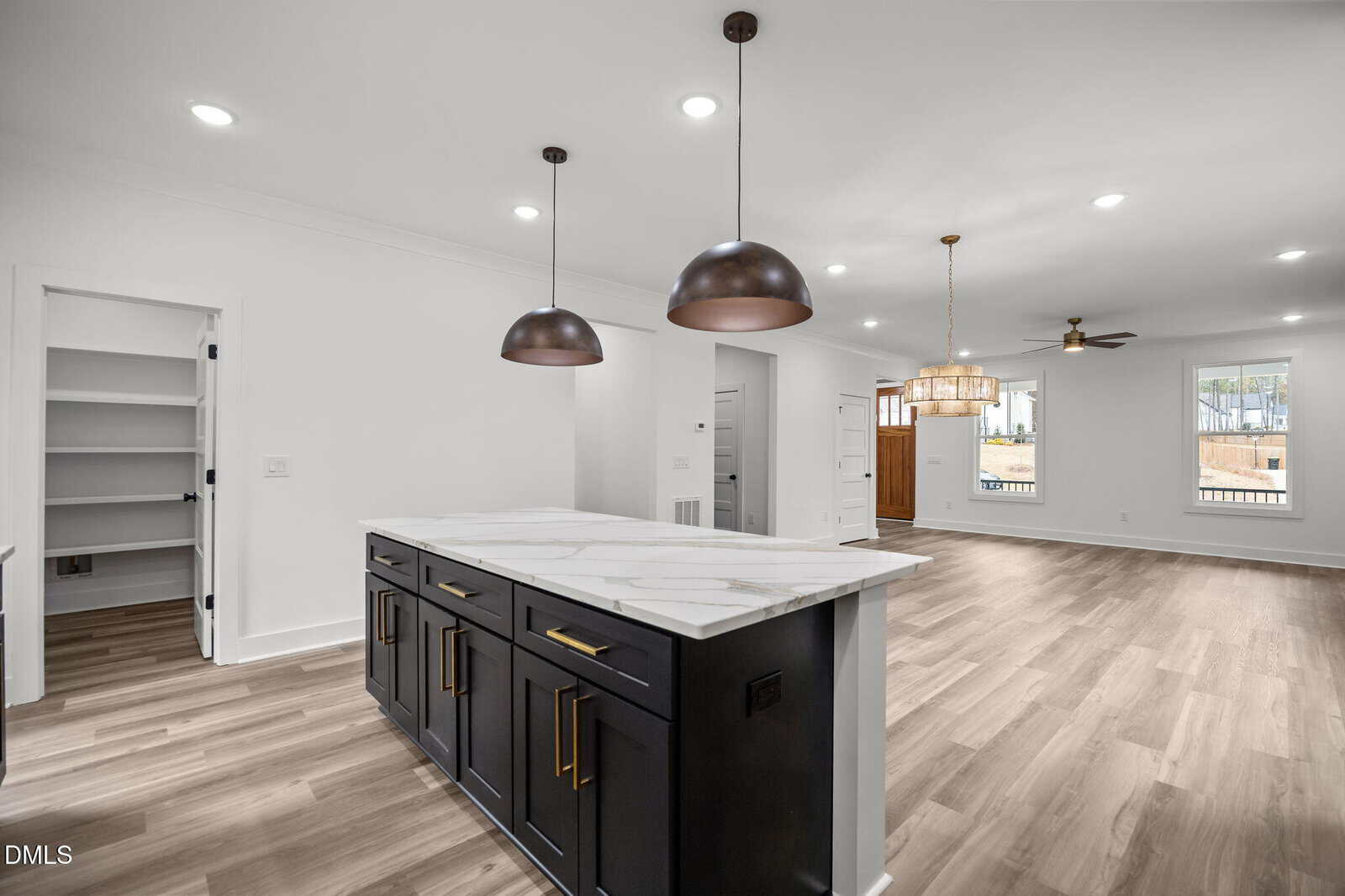 Open-concept kitchen and living area with marble island, black cabinets, two pendant lights, wood flooring, walk-in pantry, ceiling fan, and large windows letting in natural light.
