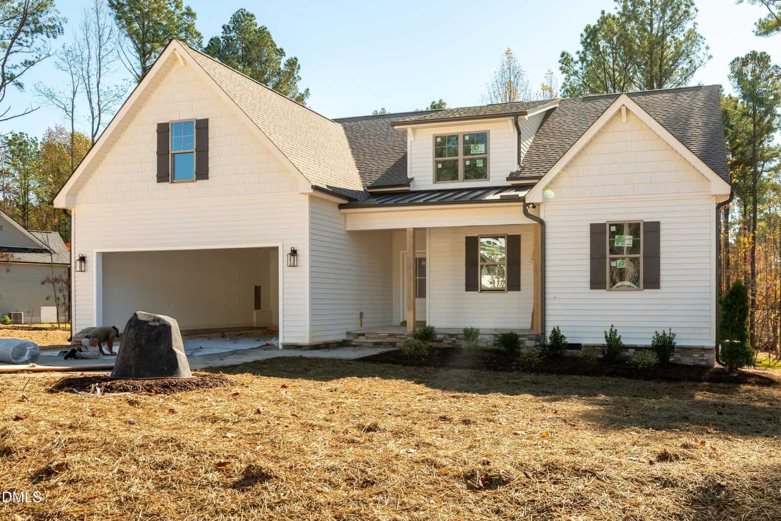 A modern two-story white house with dark shutters, a covered front porch, and an attached two-car garage awaits you at 145 Purslane Drive in Franklinton. The yard features straw covering the ground and a few small shrubs planted near the foundation, adding charm to this inviting property.