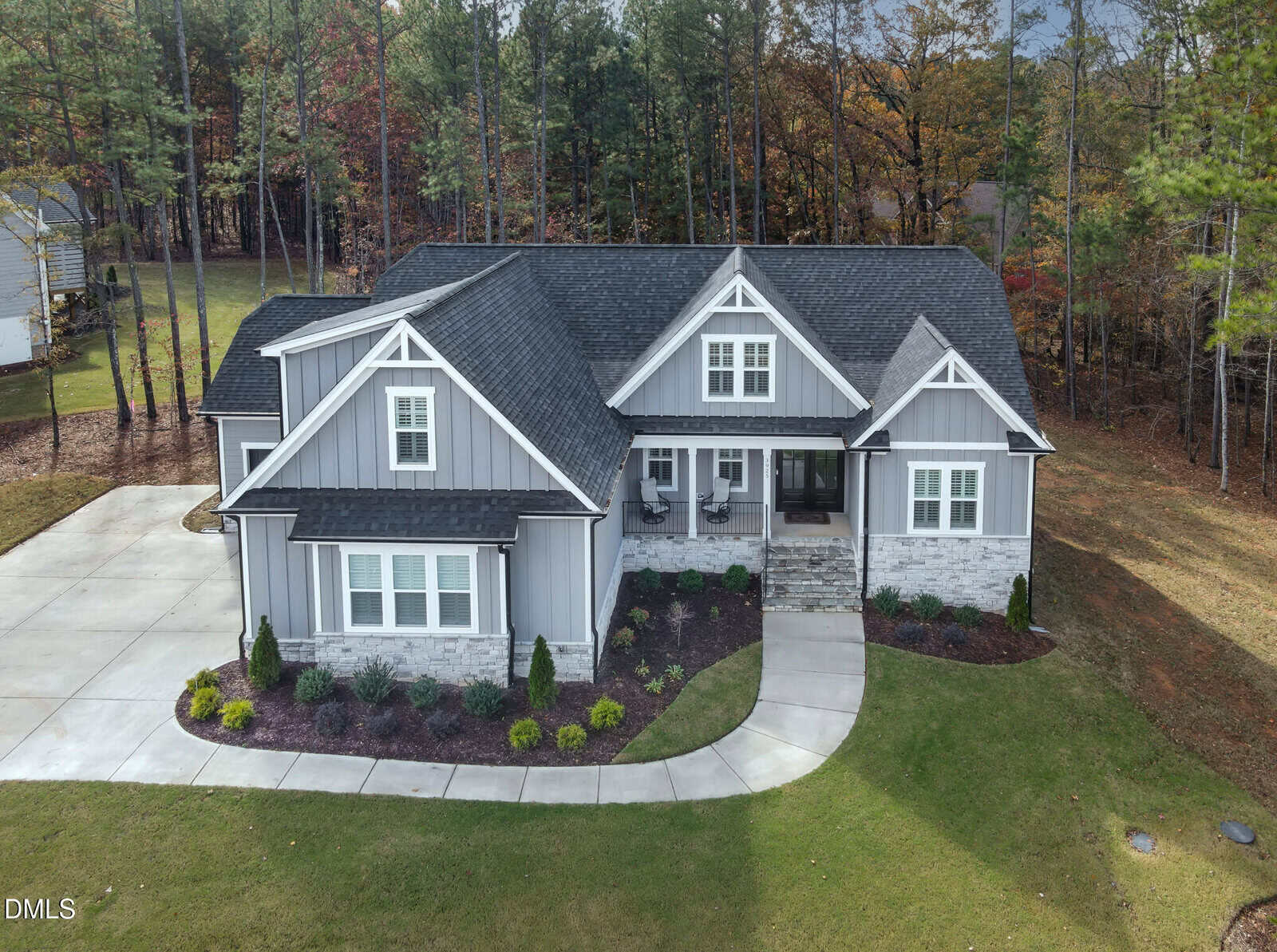 A gray, single-story house with white trim and a black roof sits on a landscaped lot with a driveway, front porch, and a curved sidewalk; trees and grass surround the property.