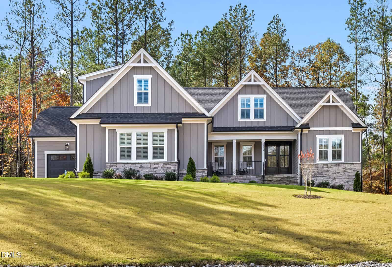 A modern suburban house with gray siding, white trim, and a front porch sits on a neatly manicured lawn at 3925 Cedar Knolls Drive in Youngsville. Tall pine trees and autumn foliage are visible in the background.