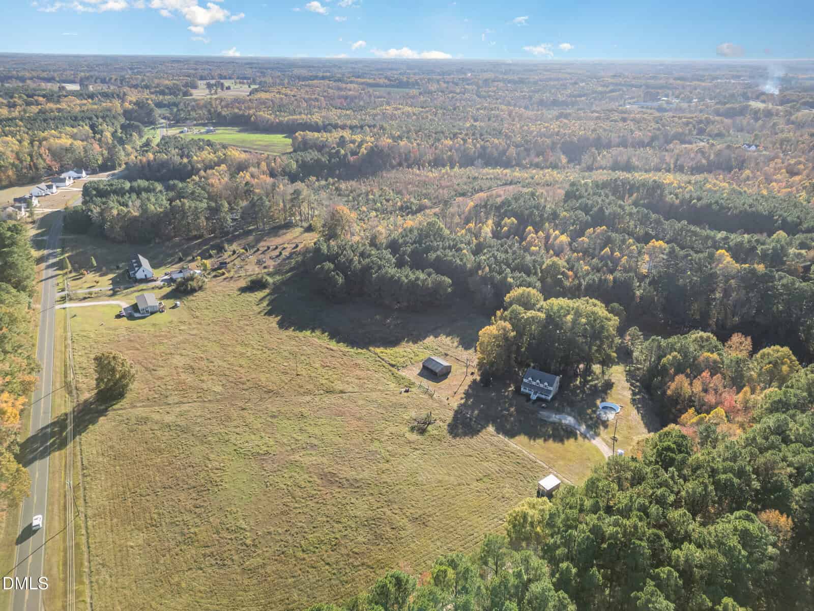Aerial view of a rural landscape near 378 Mulberry Road in Spring Hope, with open fields, scattered houses, a winding road, clusters of trees, and a mix of green and autumn foliage under a clear blue sky.