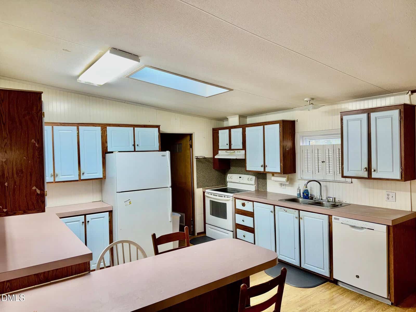 A kitchen with wood cabinets featuring light blue doors, white appliances including a fridge and stove, a double sink, ample counter space, wood flooring, and fluorescent ceiling lights.