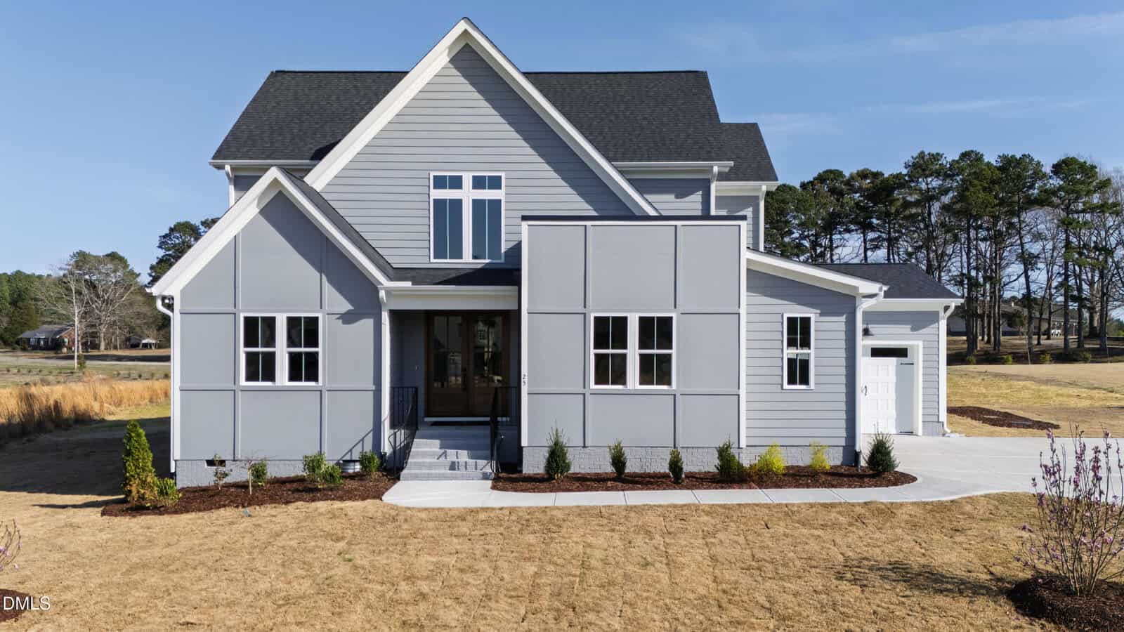 Two-story modern house with gray siding, large windows, and a black roof. Located at 25 Wheatfield Lane in Youngsville, it features a front porch with steps, neatly trimmed bushes along the walkway, and a dry, brown lawn. Trees are visible in the background.