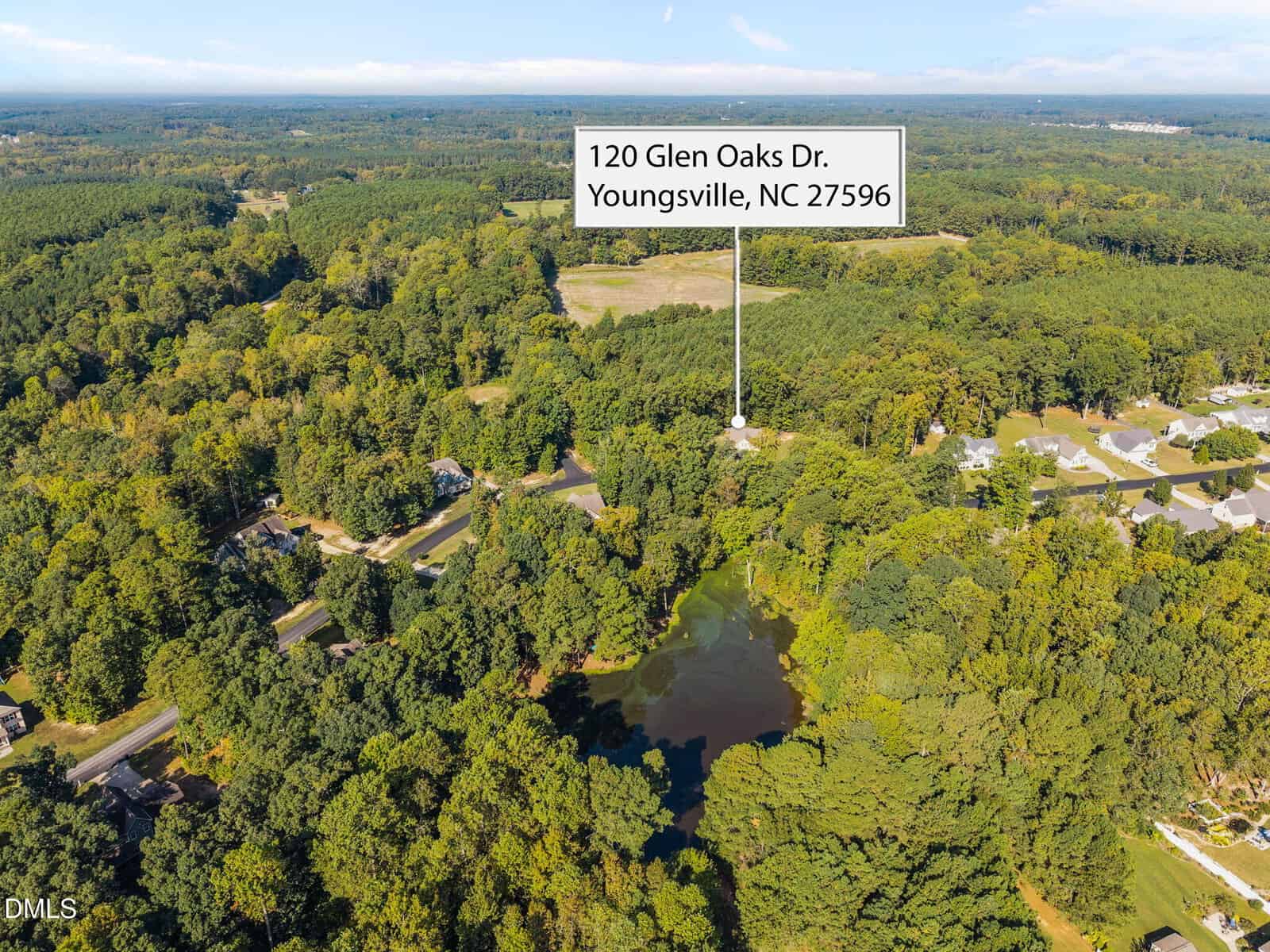 Aerial view of a wooded area with a pond and nearby houses. A label points to a property marked "120 Glen Oaks Dr. Youngsville, NC 27596." The landscape features dense trees and open fields.