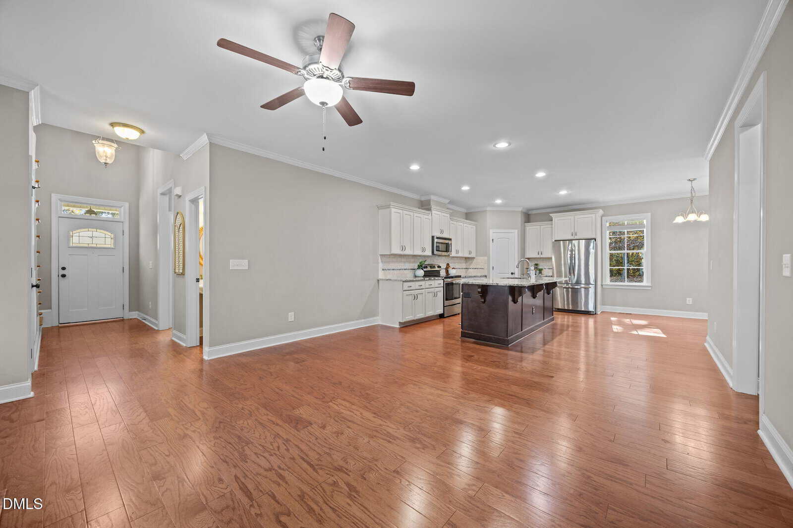 Spacious open-concept kitchen and living area with hardwood floors, ceiling fan, white cabinets, stainless steel appliances, island, and plenty of natural light from large windows.