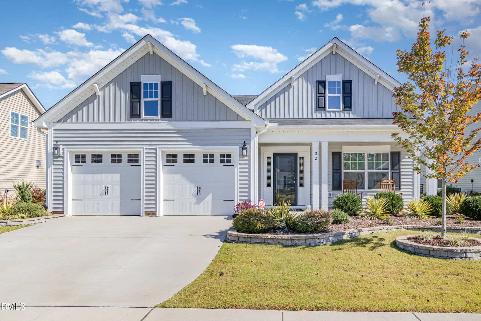 A modern, single-story house at 32 Waterclover Path in Youngsville features gray siding, two garage doors, a covered front porch with chairs, a landscaped front yard, and a small tree in the lawn under a partly cloudy sky.