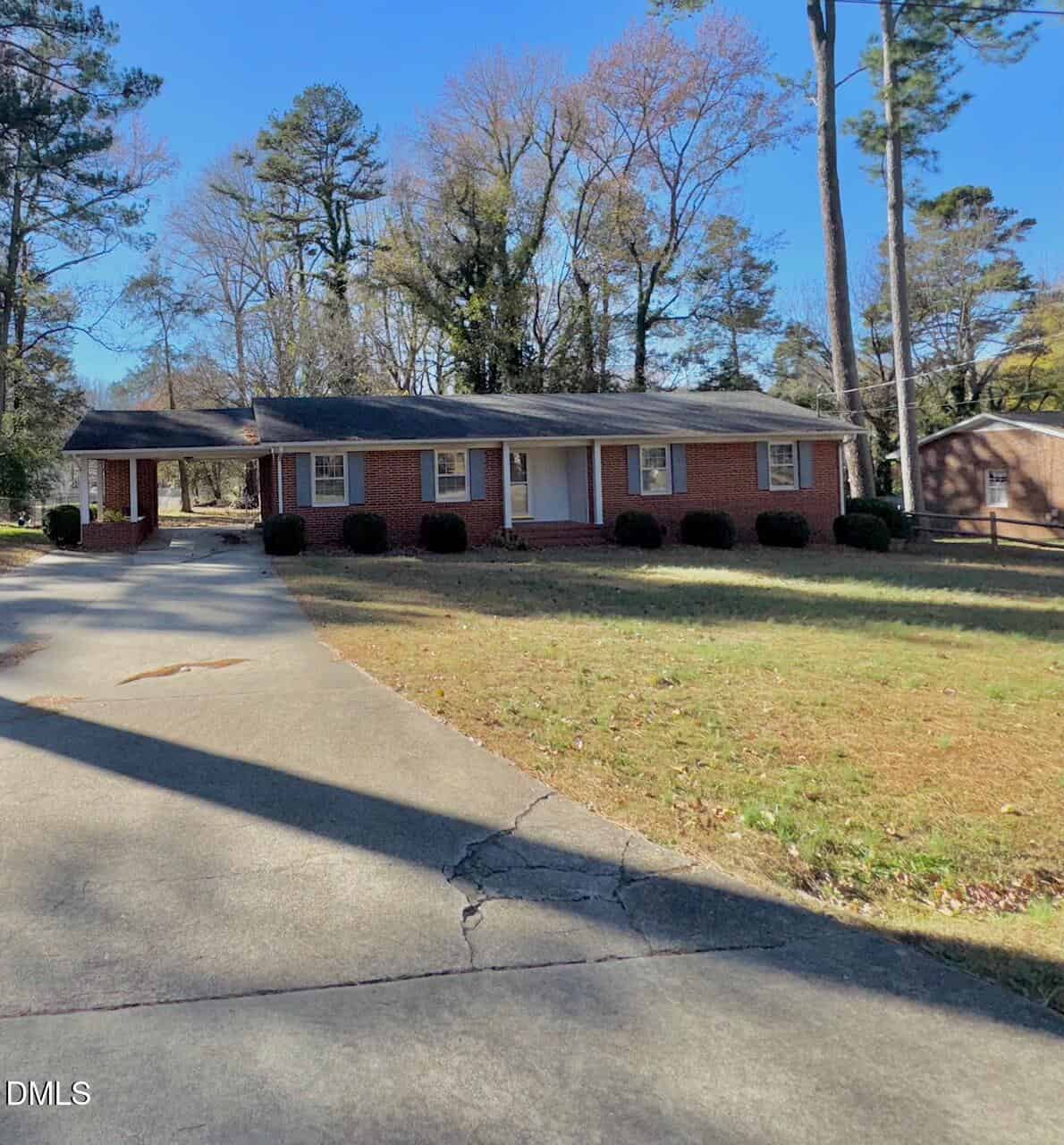 Charming single-story brick house at 146 Dorsey Place, Henderson, featuring a front porch, left-side carport, and curved driveway. The grassy lawn is accented by tall trees and shrubs, all under a clear and sunny sky.